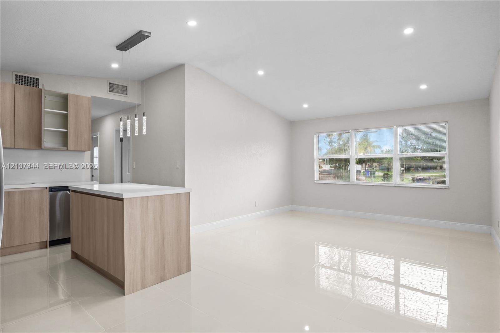 Kitchen featuring light wood-finish cabinetry, a central island with a white countertop, polished tile flooring, recessed ceiling lighting, and large windows