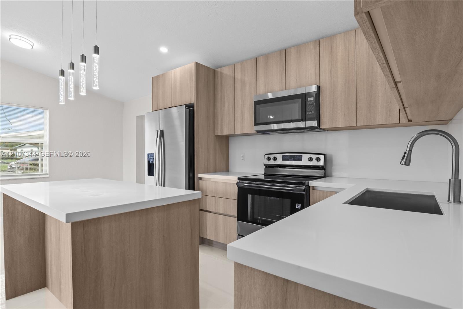 Kitchen featuring flat-panel wood-finish cabinetry, white solid-surface countertops, stainless steel appliances, a center island, and pendant lighting