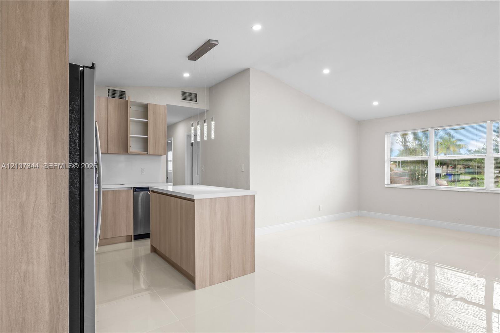Open-concept kitchen featuring light wood-finish cabinetry, a central island with a white countertop, recessed lighting, and polished tile flooring