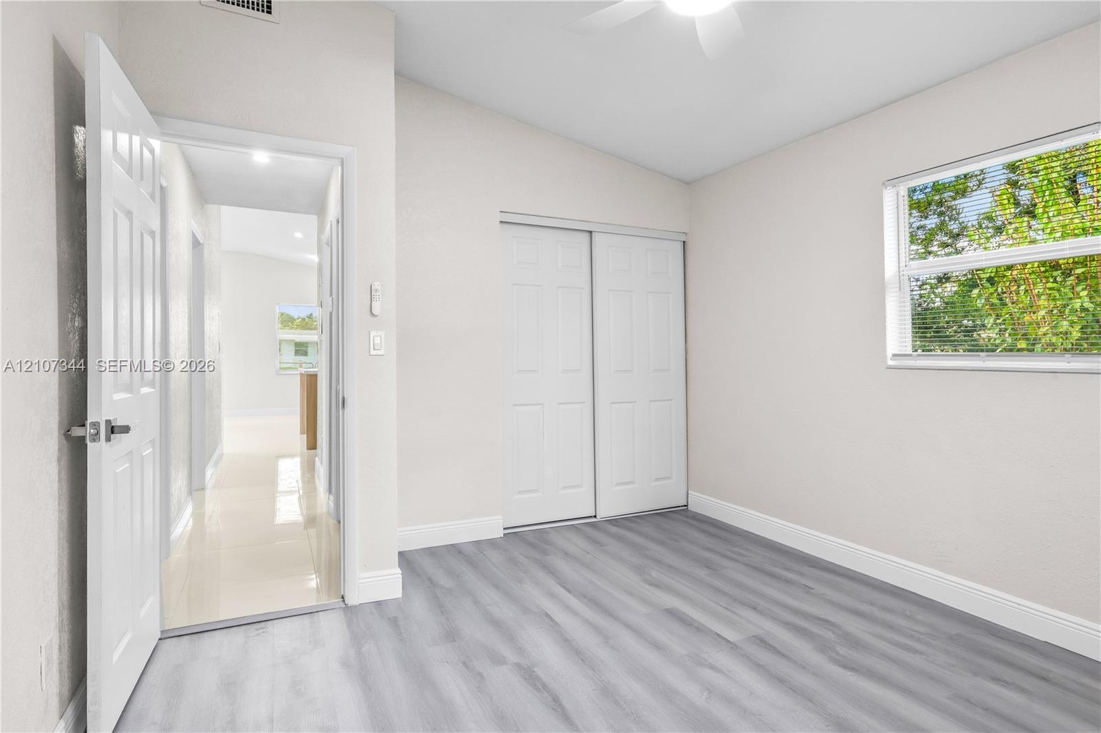 Interior room featuring wood-finish flooring, a ceiling fan, a window with horizontal blinds, and a closet with double sliding doors