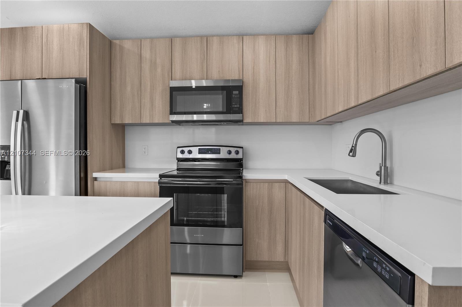 Kitchen featuring wood-finish flat-panel cabinetry, white solid-surface countertops, stainless steel appliances, and a high-arch gooseneck faucet