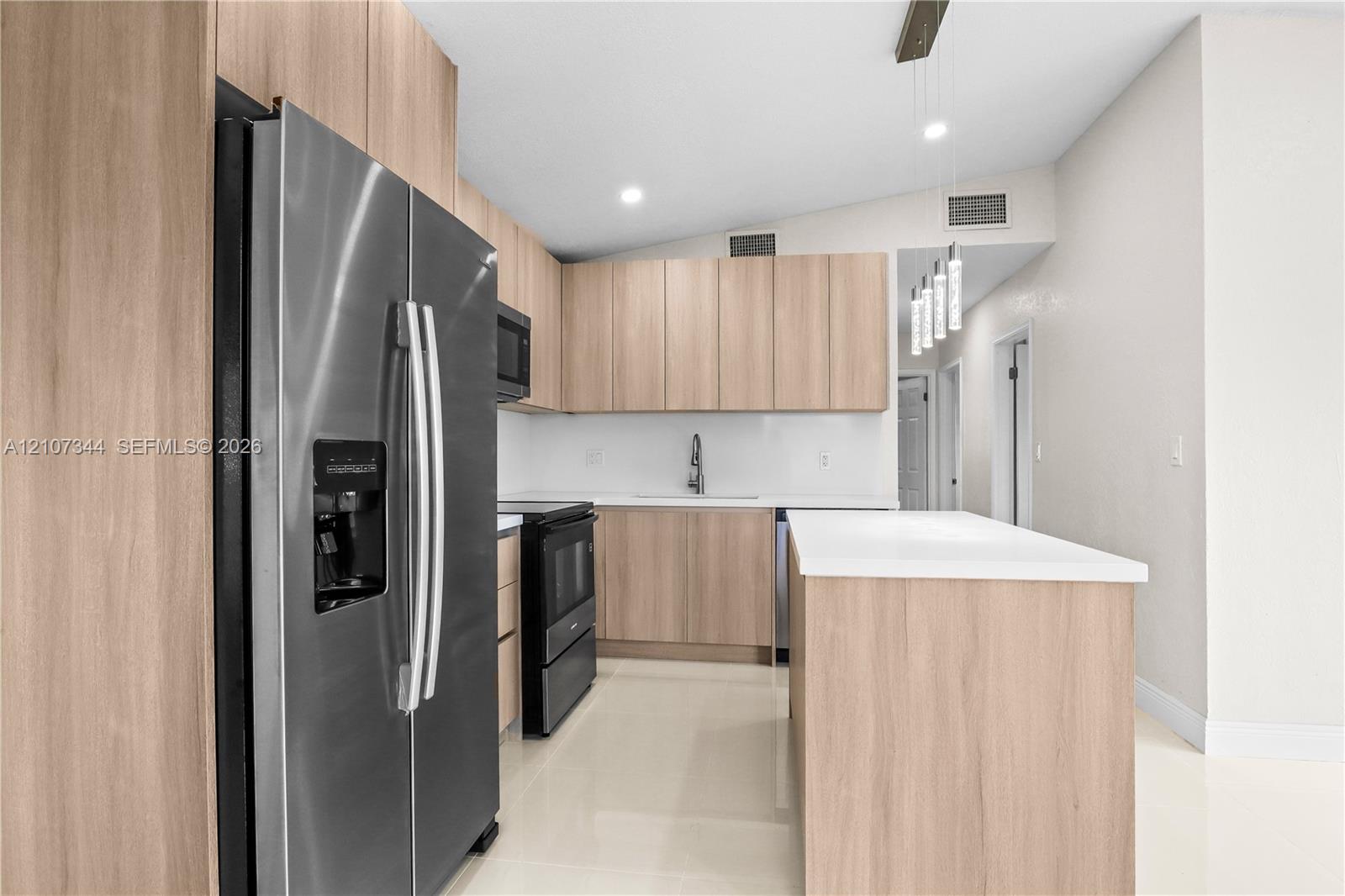 Kitchen featuring wood-finish cabinetry, a center island with a quartz countertop, stainless steel appliances, and pendant lighting