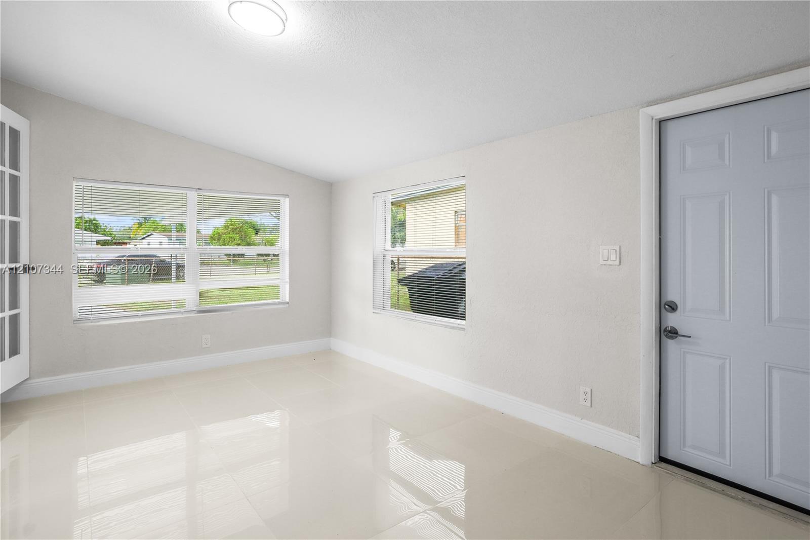 Neutral-toned interior featuring large-format tile flooring, multiple windows, a multi-panel entry door, and a multi-lite French door