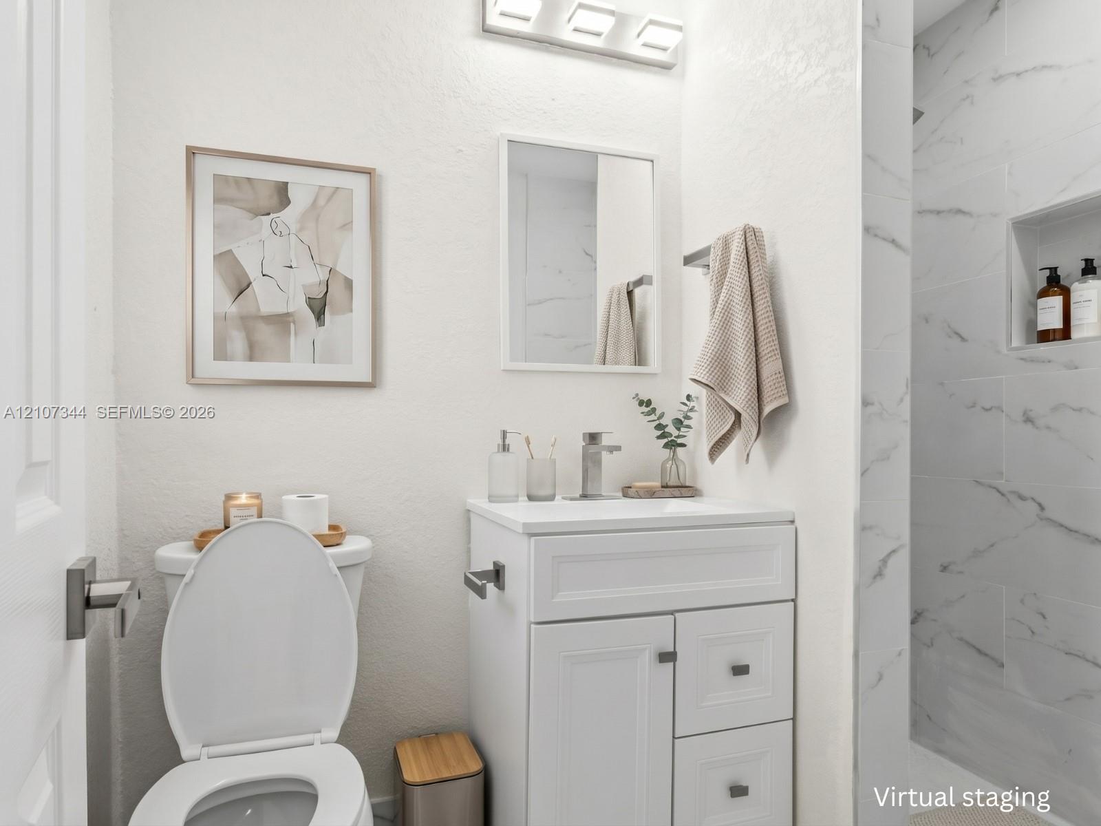Bathroom vanity with white cabinetry and a rectangular sink, brushed nickel faucet, wall-mounted light fixture, and shower surround with stone-finish tile and a built-in recessed niche