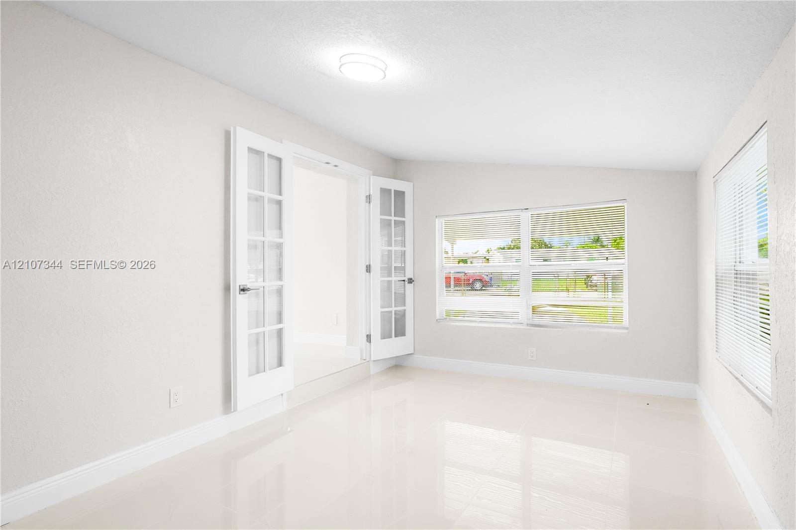 Bright interior featuring polished tile flooring, white French doors with glass panes, flush-mount ceiling lighting, and large windows with horizontal blinds