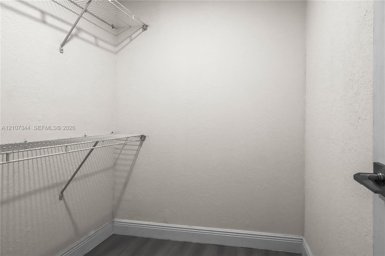 Storage space featuring dual-tier white wire shelving and grey wood-finish flooring