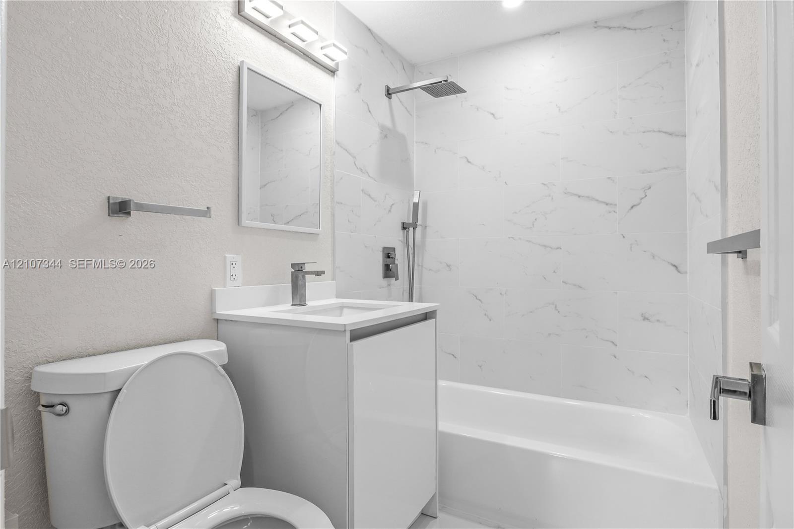 Bathroom featuring a full-height tile surround with a marble-finish pattern, a sleek white vanity with a rectangular sink, wall-mounted modern faucet hardware, and a rainfall shower head