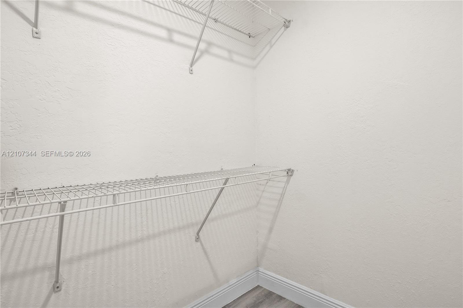 Storage area featuring white textured walls and dual-tier white wire shelving systems