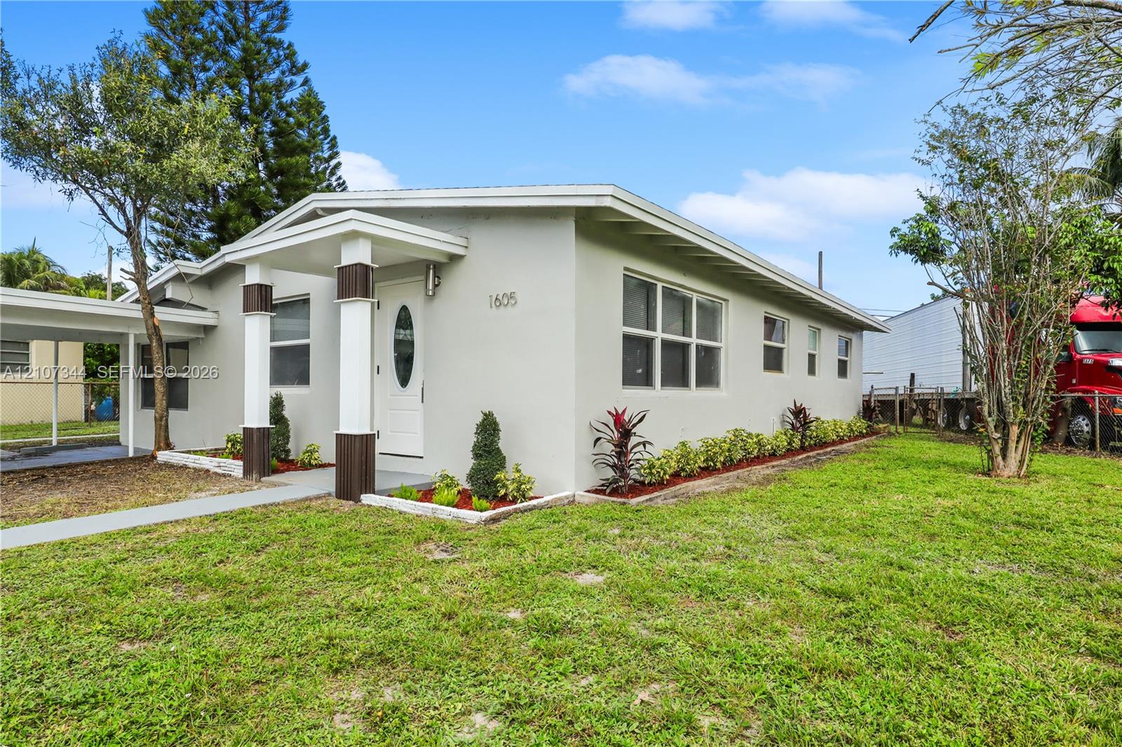 Single-story exterior featuring a covered front entry with architectural columns, a dedicated side carport, smooth-finish siding, and a landscaped front garden bed