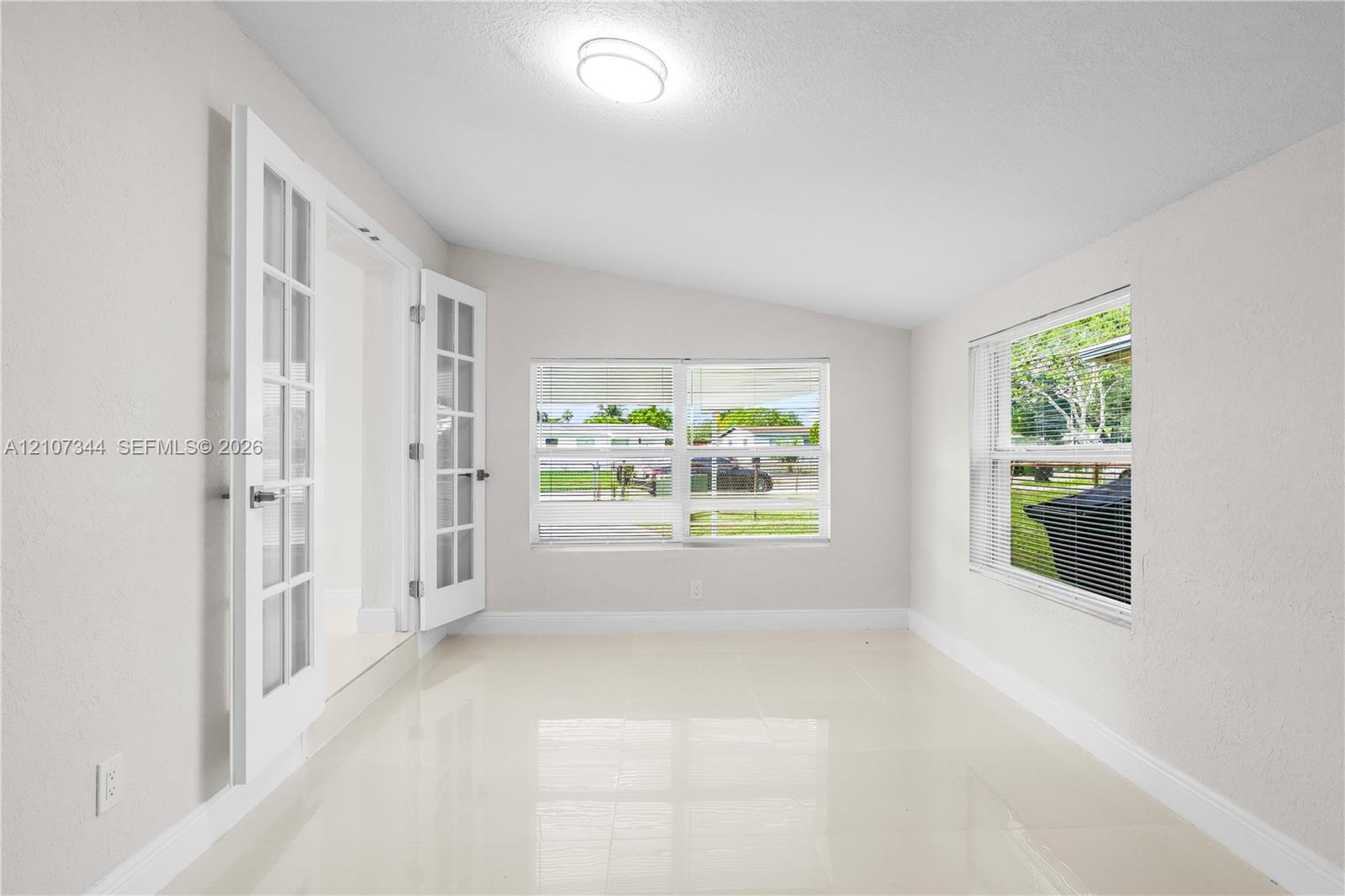 Bright sunroom featuring light-toned tile flooring, white-painted walls, dual French doors with glass panes, and large picture windows