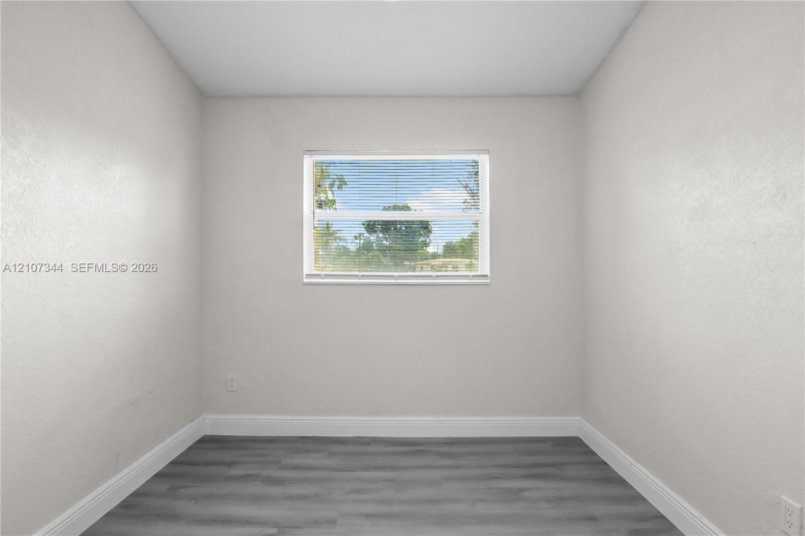 Interior space featuring neutral-toned walls, wood-finish flooring, and a central window with horizontal blinds