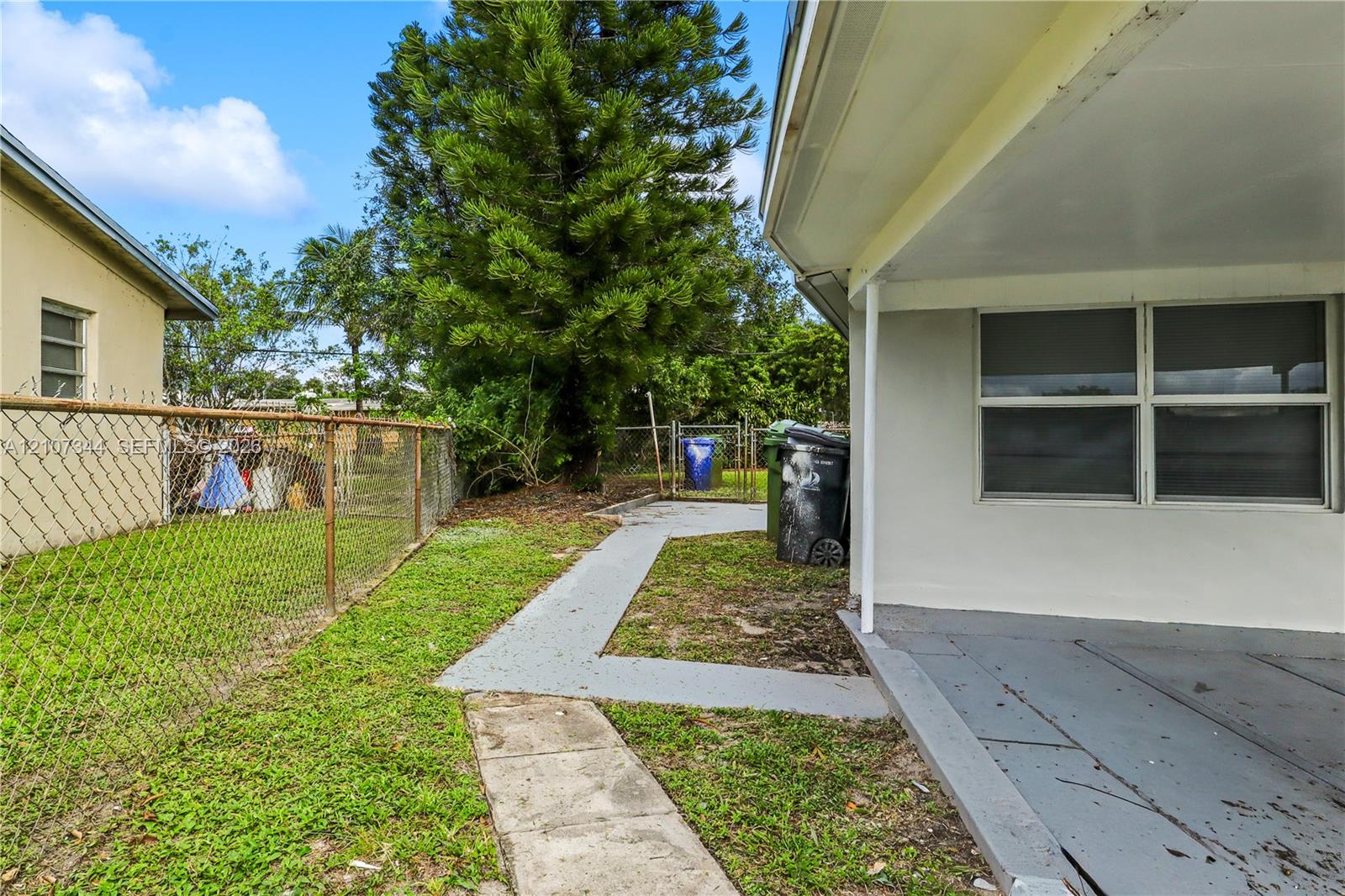 Covered rear patio featuring a concrete floor, painted masonry exterior walls, and a perimeter chain-link fence