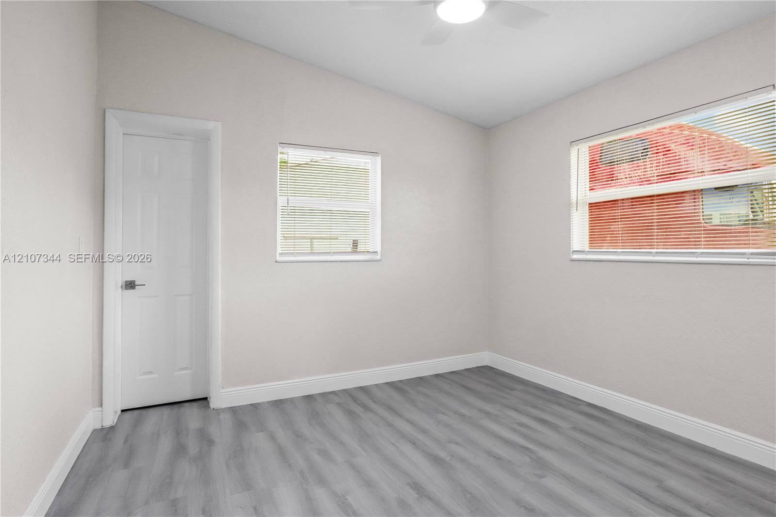 Interior room featuring vaulted ceilings, wood-finish flooring, two windows with integrated blinds, and a ceiling-mounted light fixture