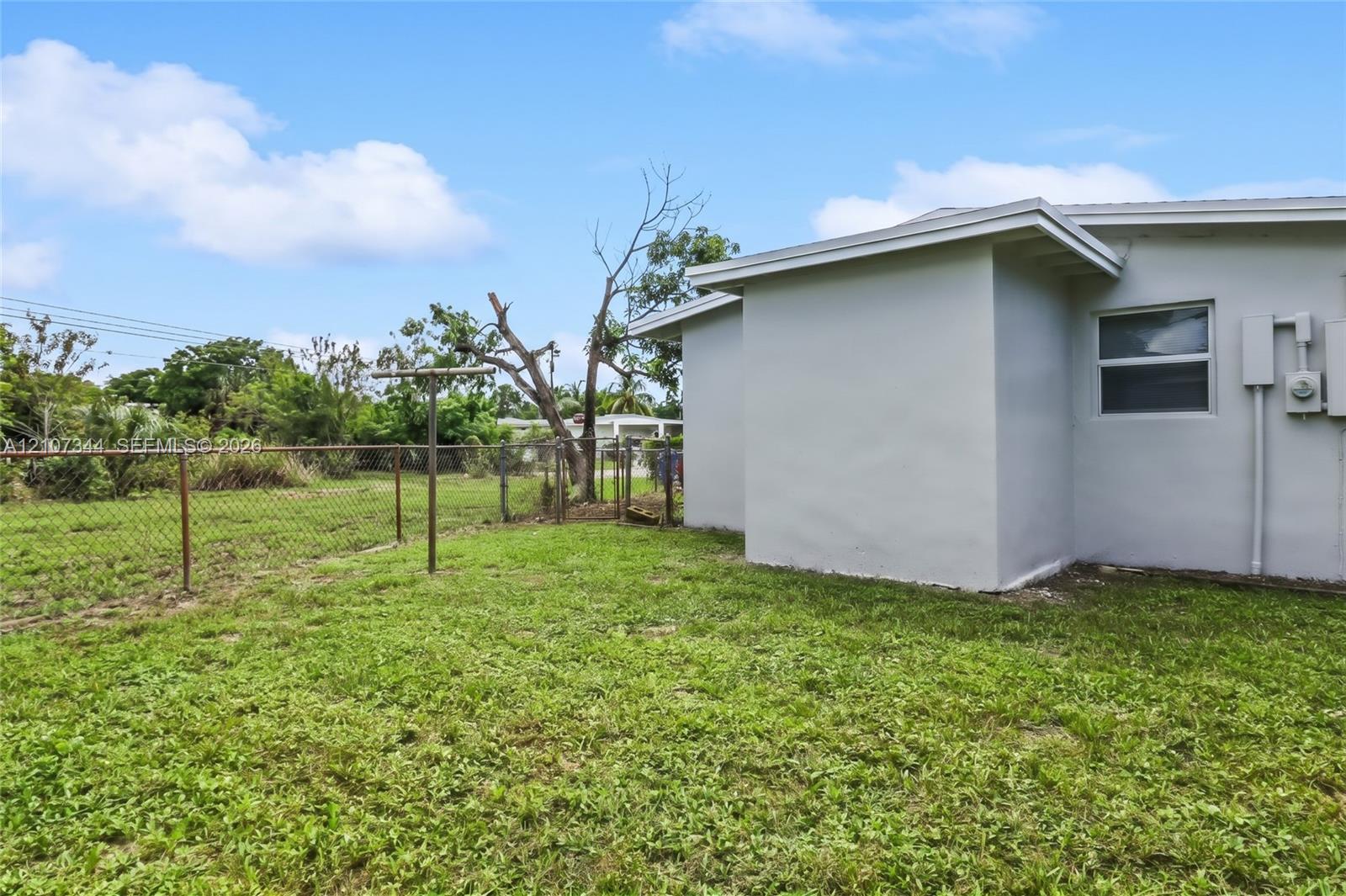 Exterior featuring a light-toned stucco finish, single-hung window, chain-link perimeter fencing, and open greenspace