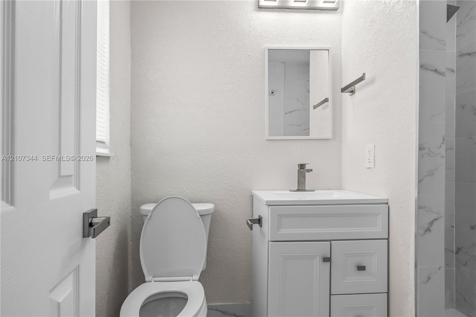 White vanity with integrated basin, single-handle faucet, rectangular wall mirror, and walk-in shower featuring tiled surround