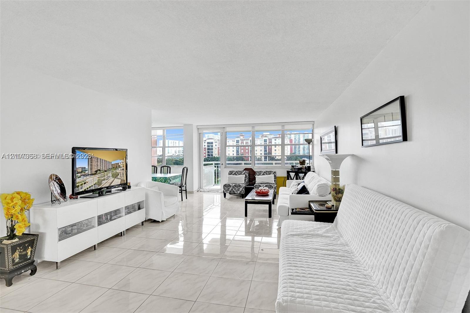 Open-concept living space featuring large-format ceramic tile flooring, floor-to-ceiling windows, and access to an exterior balcony
