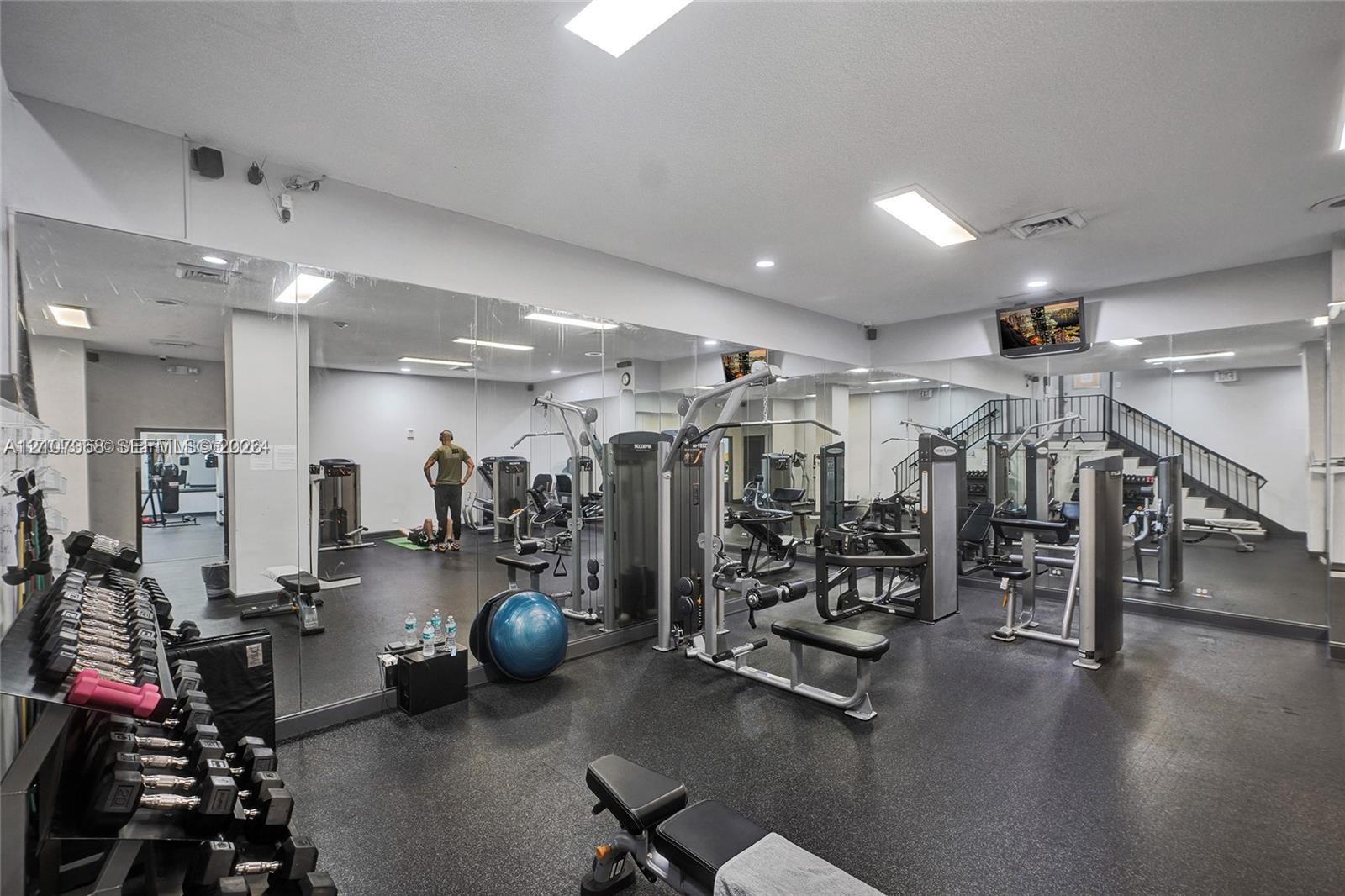 Fitness center featuring wall-to-wall mirrors, recessed lighting, and durable rubberized flooring