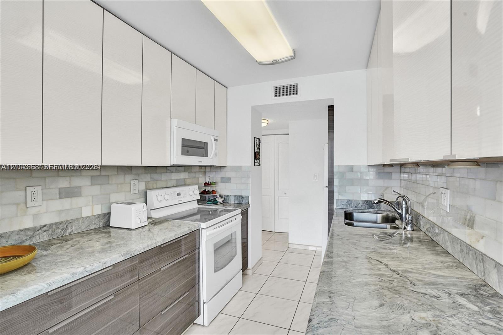 Kitchen featuring high-gloss white upper cabinetry, horizontal grain wood-finish lower cabinets, stone countertops, a subway tile backsplash, and ceramic floor tiling