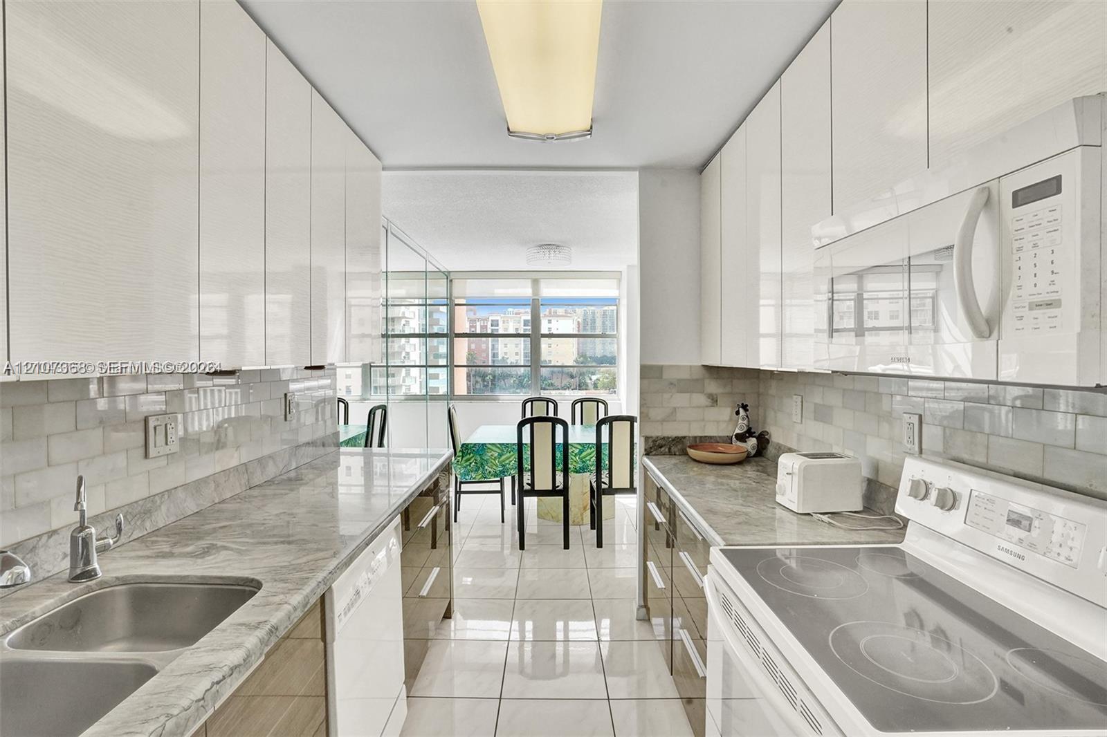 Kitchen featuring gloss-finish cabinetry, stone-finish countertops, subway tile backsplash, stainless steel double-basin sink, and tile flooring