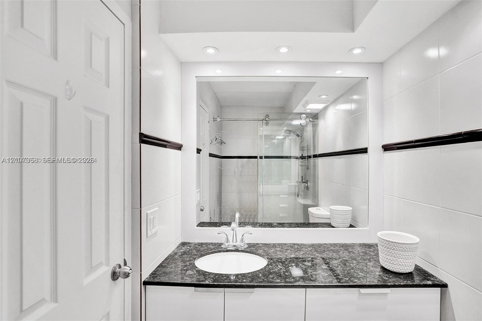 Bathroom featuring a stone-surface vanity with an integrated basin, high-gloss white cabinetry, large-format wall tiling with a dark decorative accent border, and a glass-enclosed shower stall with sliding hardware