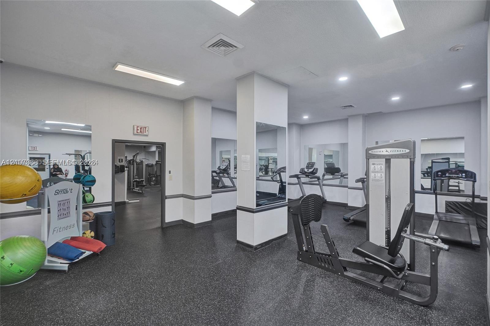 Fitness room featuring rubberized flooring, recessed ceiling lighting, wall-to-wall mirrors, and structural columns