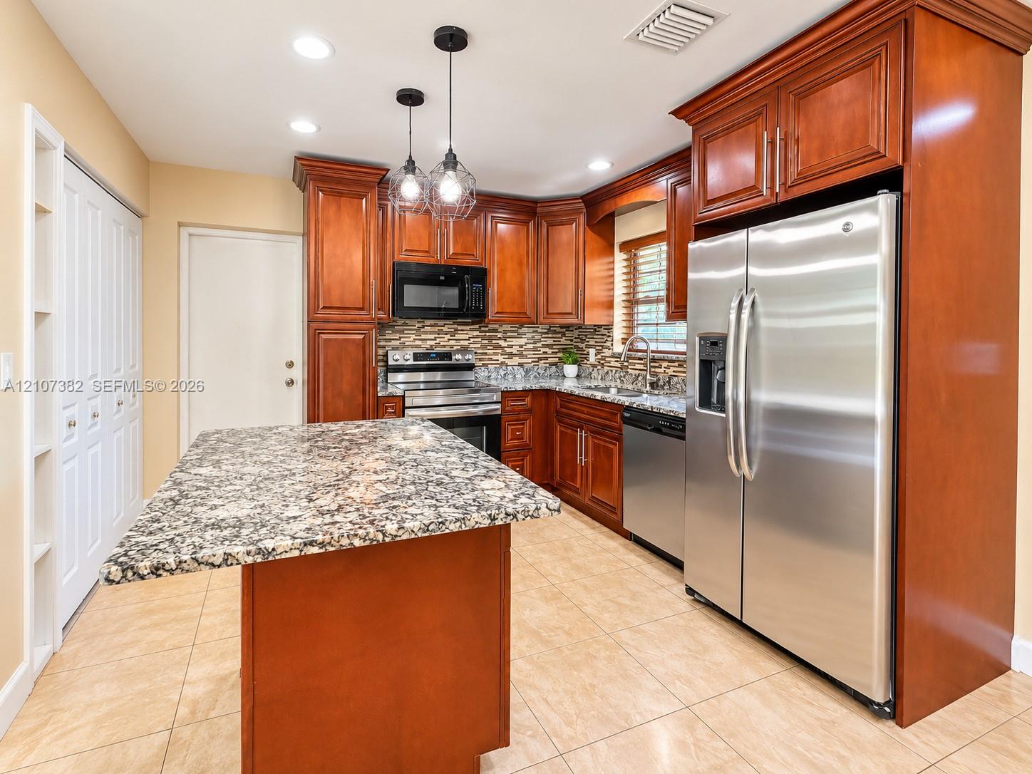 Kitchen featuring stained wood cabinetry, stone countertops, a central island, tile flooring, and stainless steel appliances