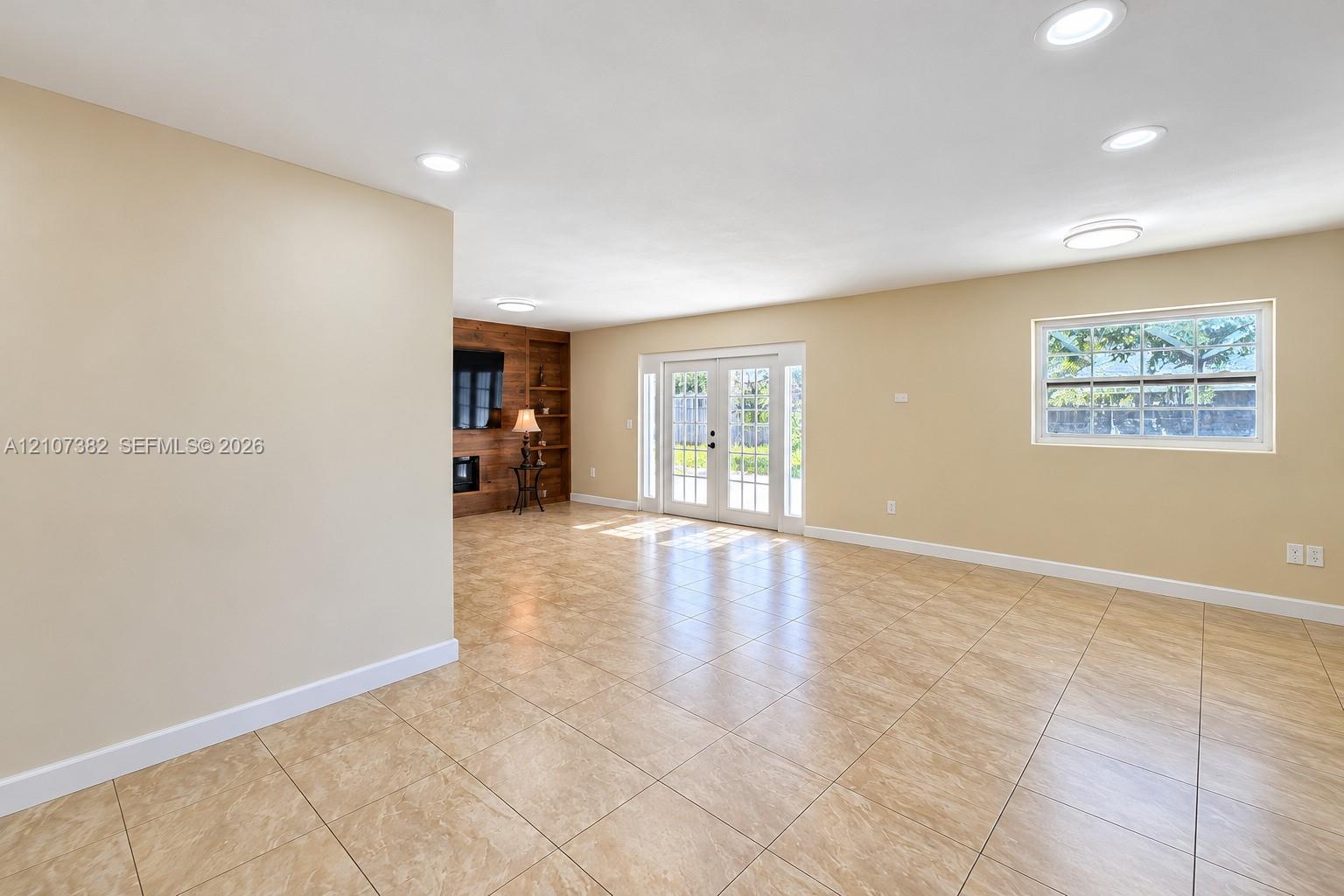 Neutral tile flooring, recessed lighting, double French doors, and a wood-paneled accent wall with a built-in fireplace