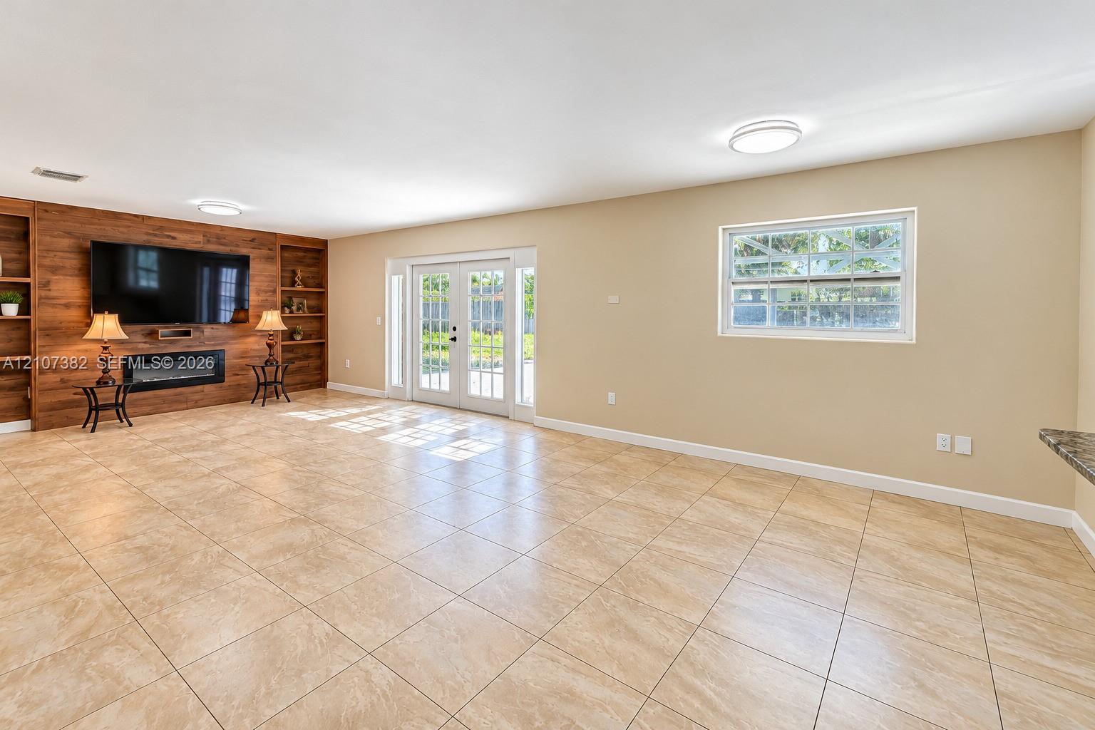 Spacious interior featuring large-format tile flooring, built-in wood-finish cabinetry, a sleek electric fireplace, and double-pane French doors
