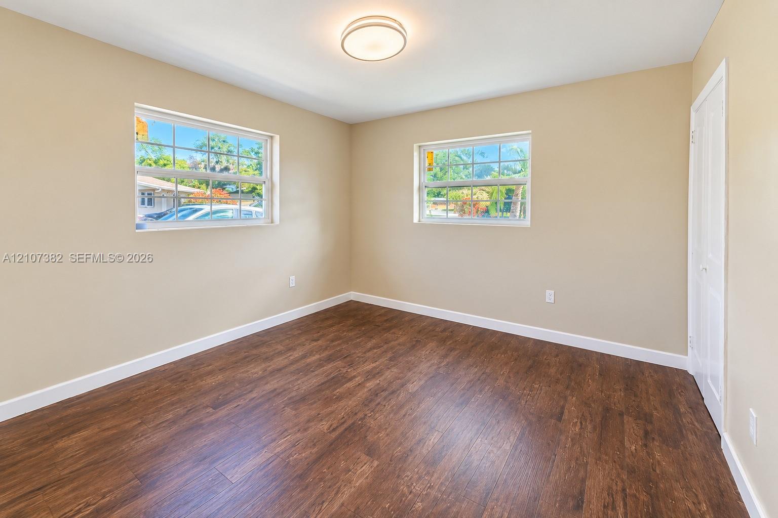 Neutral-toned interior room featuring wood-finish flooring, two dual-pane windows with muntins, and a ceiling-mounted light fixture
