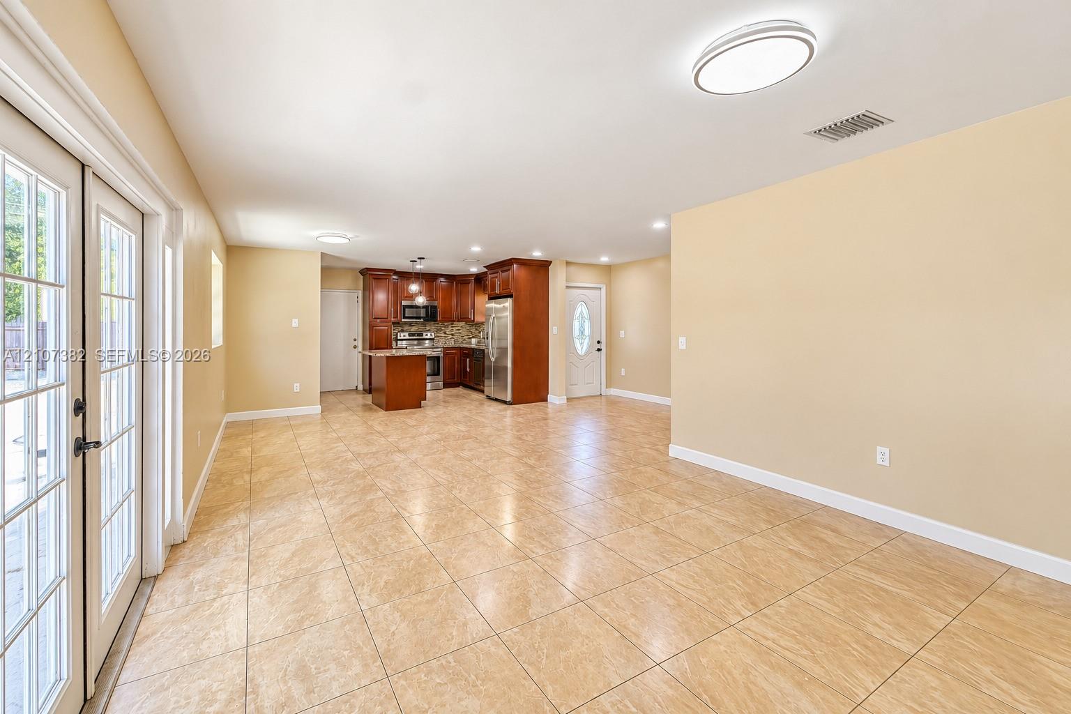 Open-concept interior featuring large-format tile flooring, recessed lighting, wood-finish cabinetry, stainless steel appliances, and glass-paned double doors