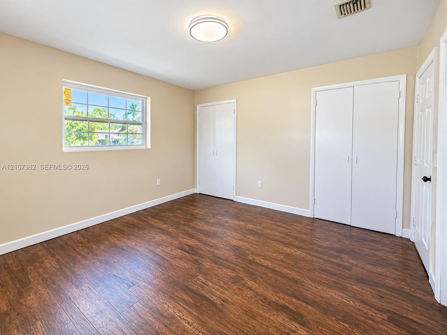 Interior room featuring wood-finish flooring, dual built-in closets with white paneled doors, and a multi-pane window