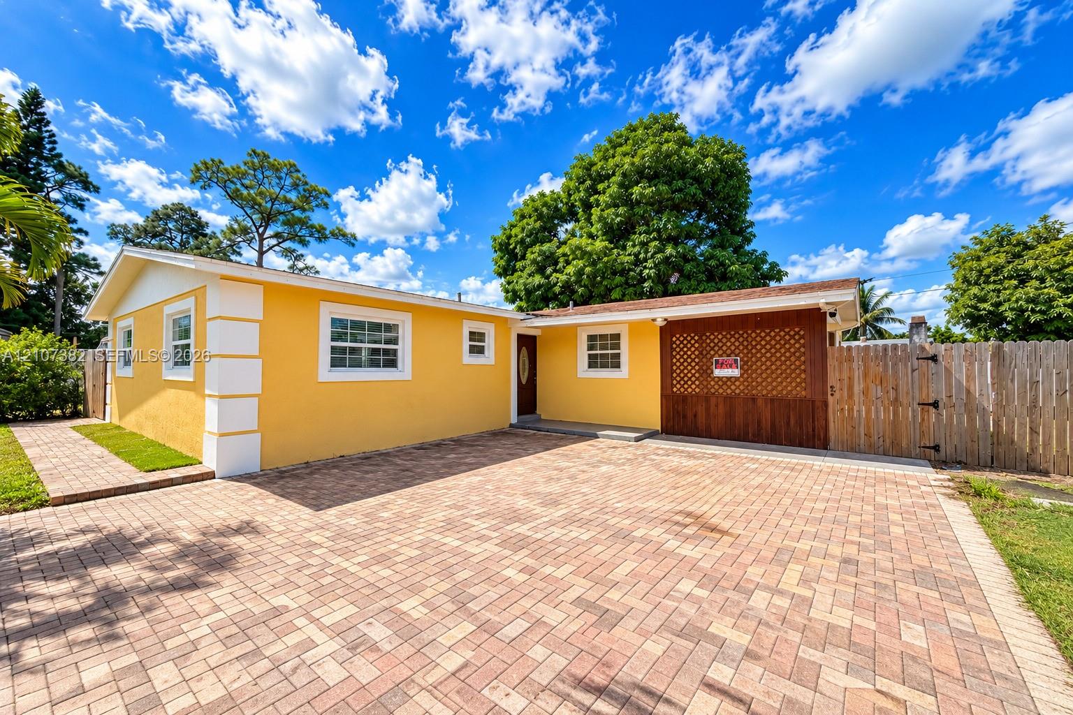 Stucco exterior featuring corner quoins, expansive paver driveway, integrated wooden lattice screen, and wood-paneled privacy fencing