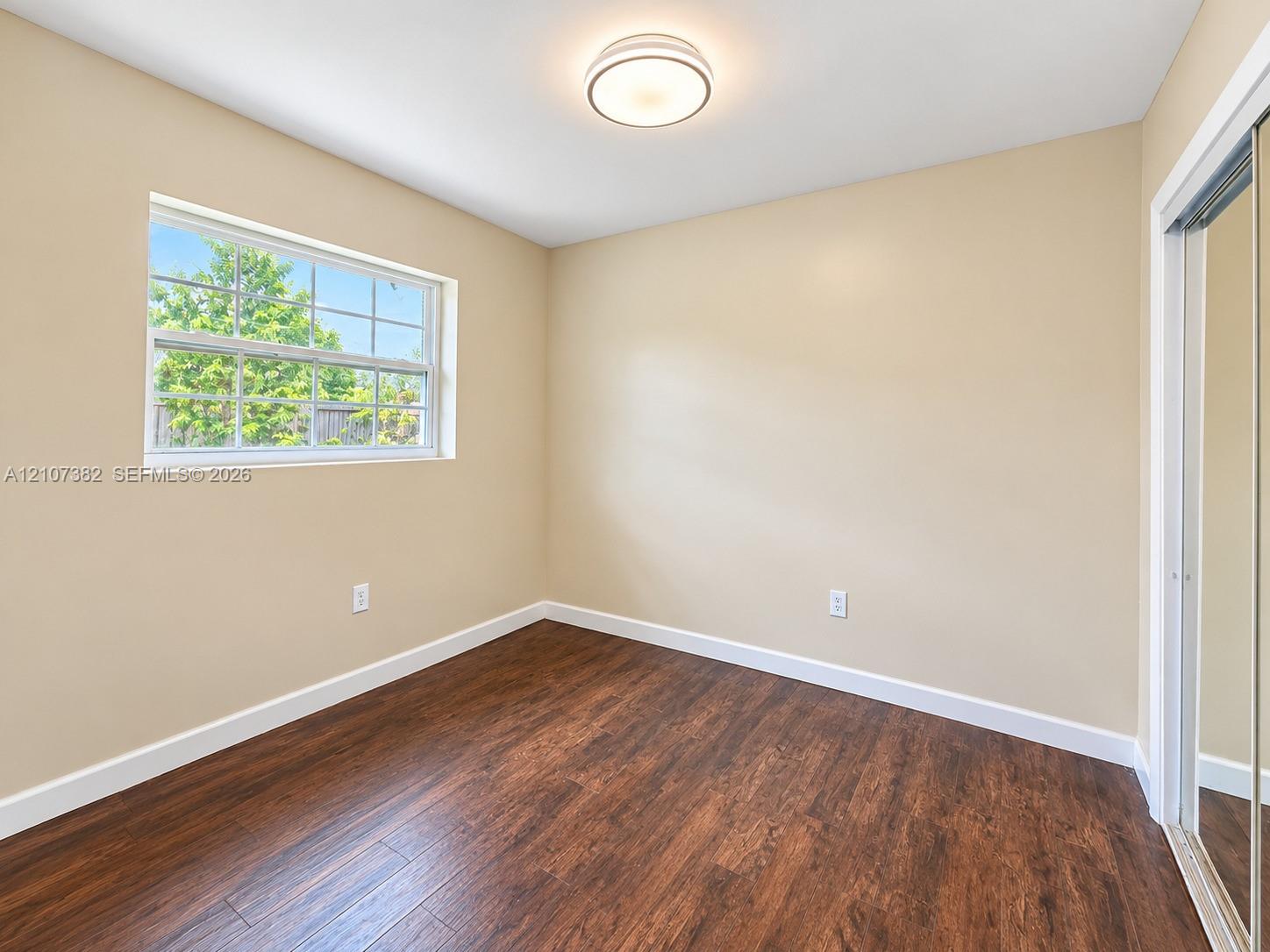Room featuring wood-finish flooring, a multi-pane window, mirrored sliding closet doors, and a flush-mount ceiling light fixture