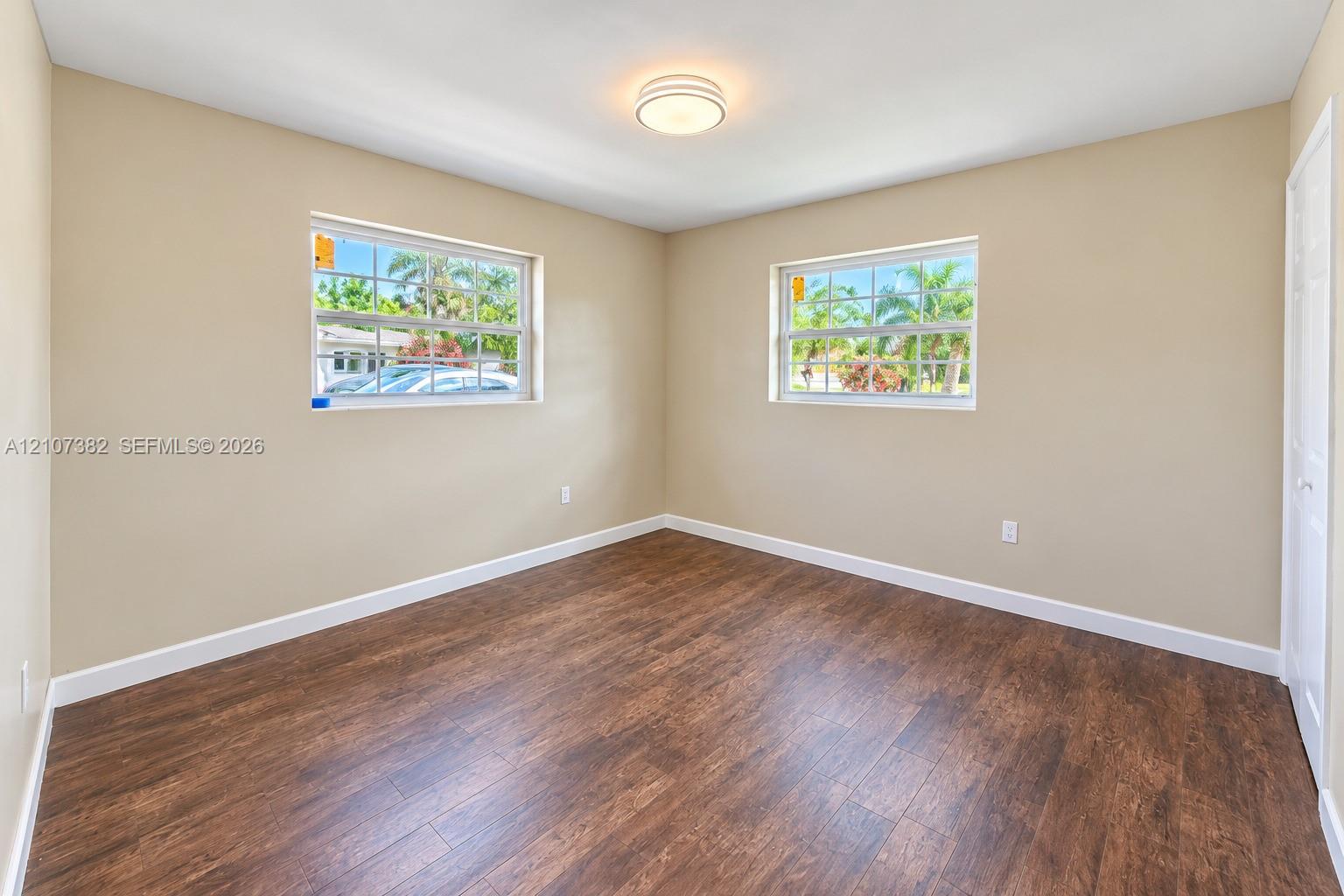 Room featuring wood-finish flooring, dual windows with grid detailing, neutral wall tones, and a central flush-mount ceiling light fixture