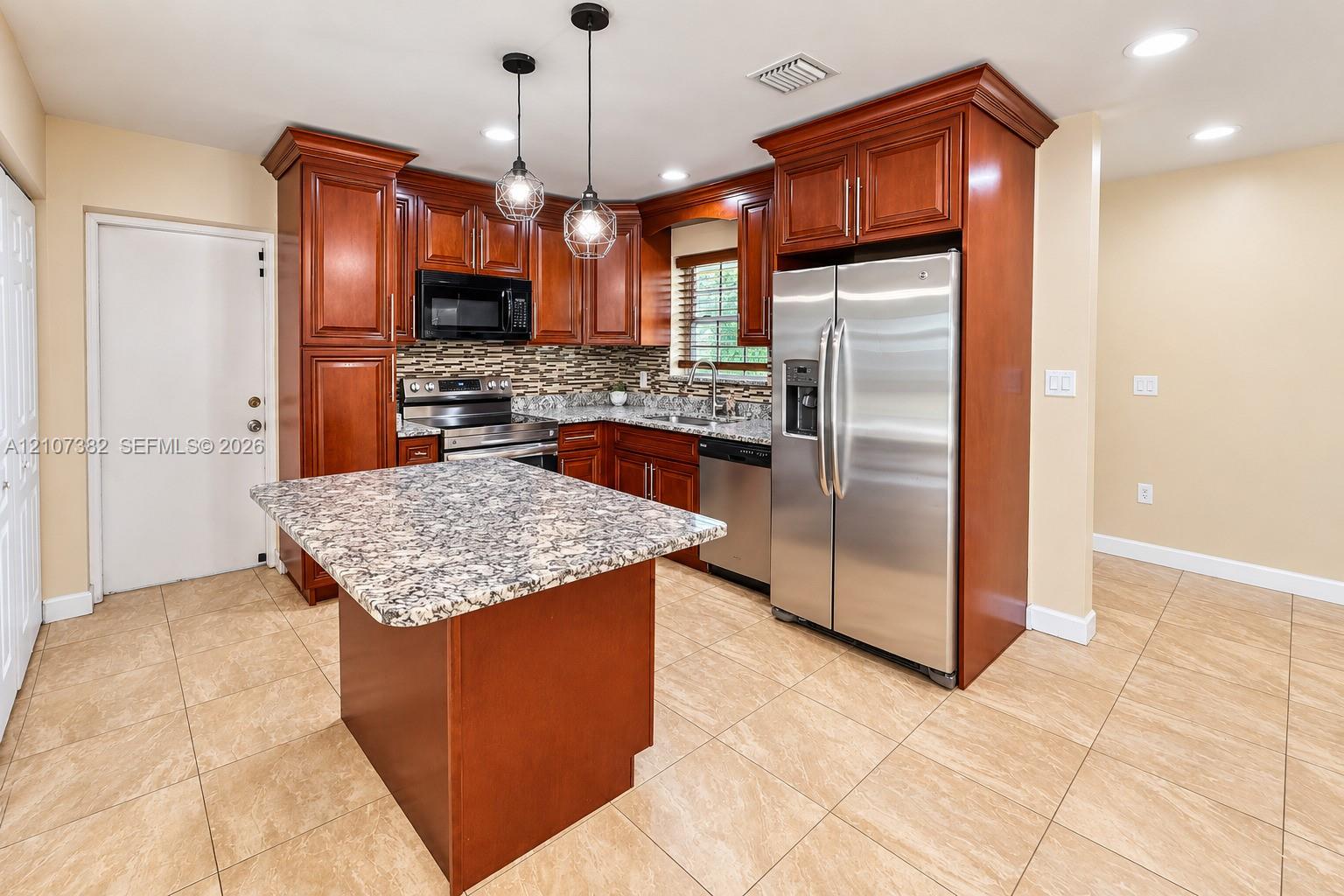 Kitchen featuring rich wood cabinetry, stone-surface countertops, stainless steel appliances, a central island, and glass pendant lighting