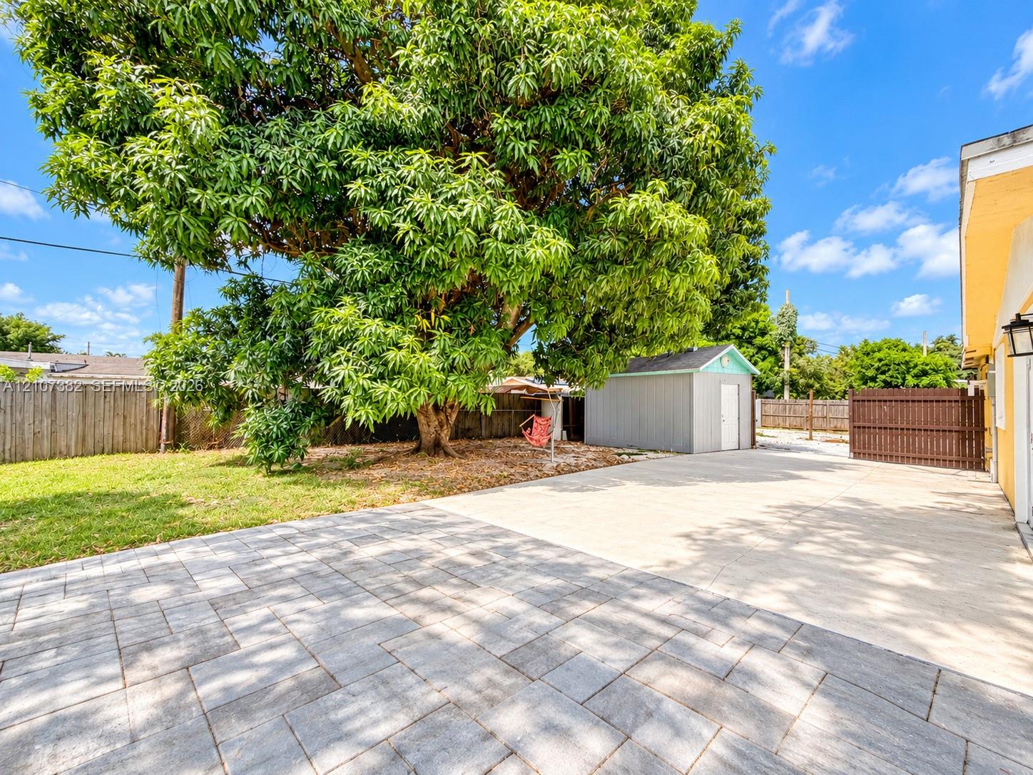Rear yard featuring a paved patio, large mature tree, detached storage structure, and fenced perimeter