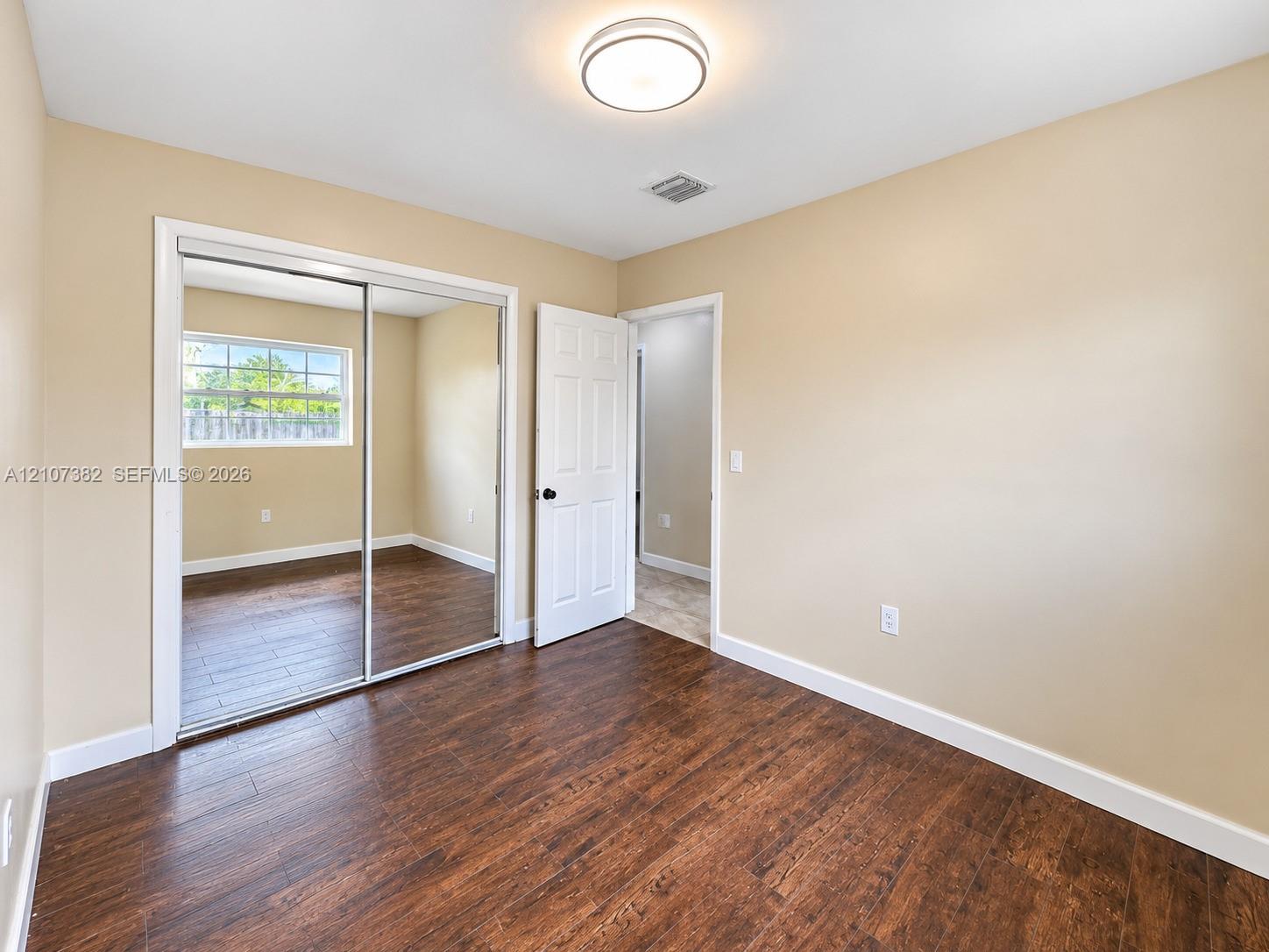 Interior room featuring wood-finish flooring, sliding mirror-panel closet doors, a multi-panel interior door, and a circular flush-mount ceiling light fixture