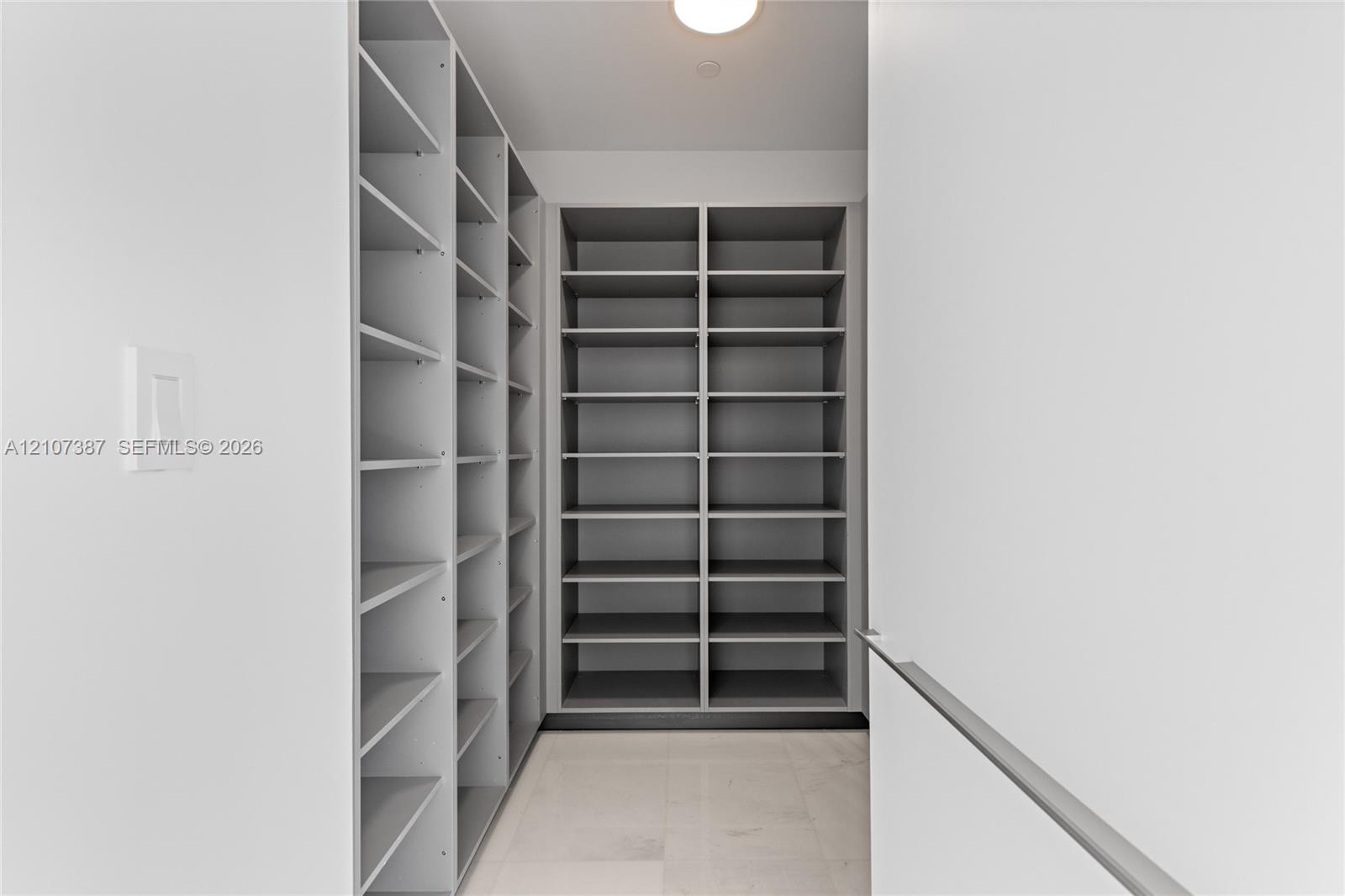 Custom walk-in storage featuring grey floor-to-ceiling shelving, light-toned tile flooring, and integrated overhead lighting