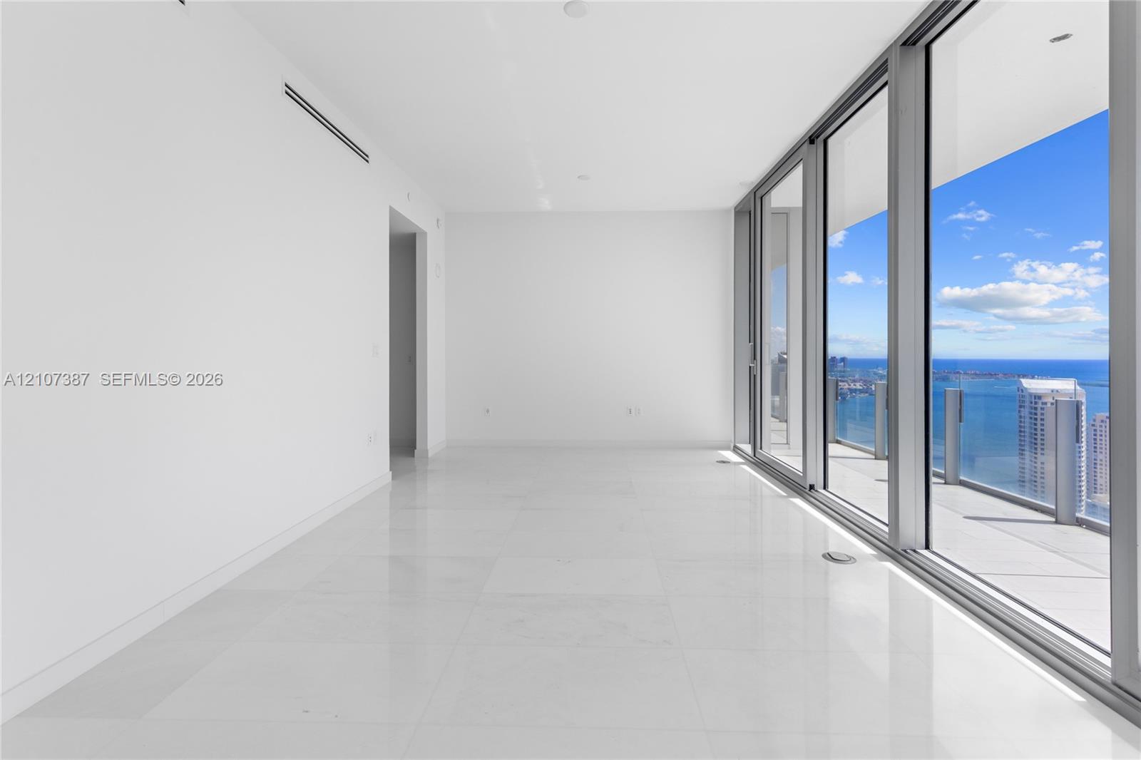 Interior space featuring floor-to-ceiling glass sliding doors, large-format tile flooring, recessed lighting, and a wrap-around balcony with glass railings