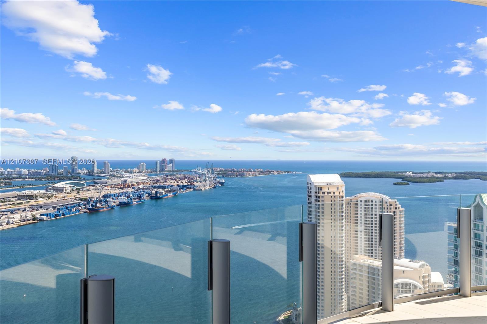 Expansive balcony featuring frameless glass railings and paved flooring, showcasing a panoramic coastal, harbor, and cityscape backdrop
