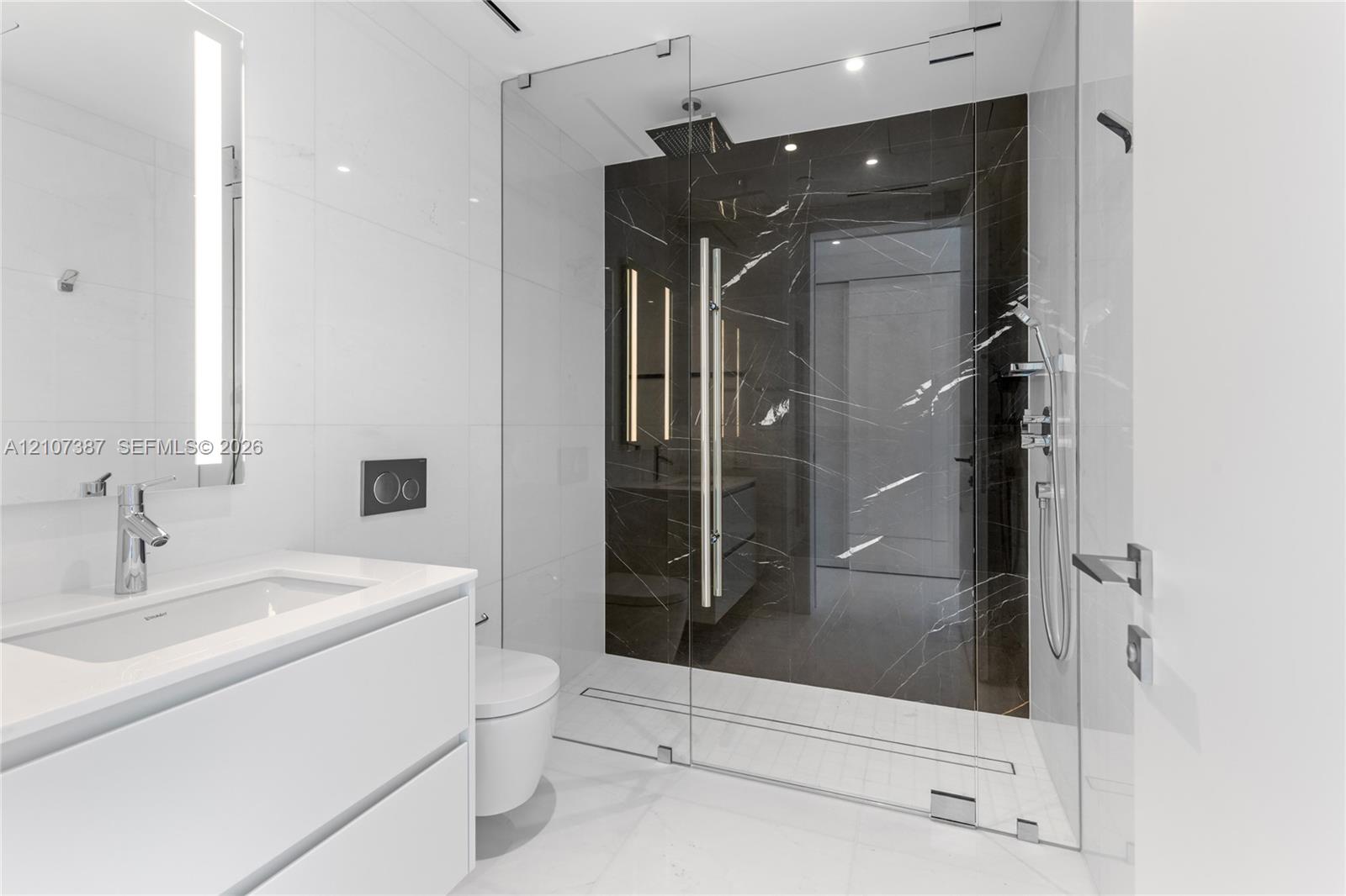 Modern bathroom featuring a floating white vanity with a rectangular sink, wall-mounted faucet, walk-in shower with floor-to-ceiling glass enclosure, dark stone-finish shower surround, and integrated lighting