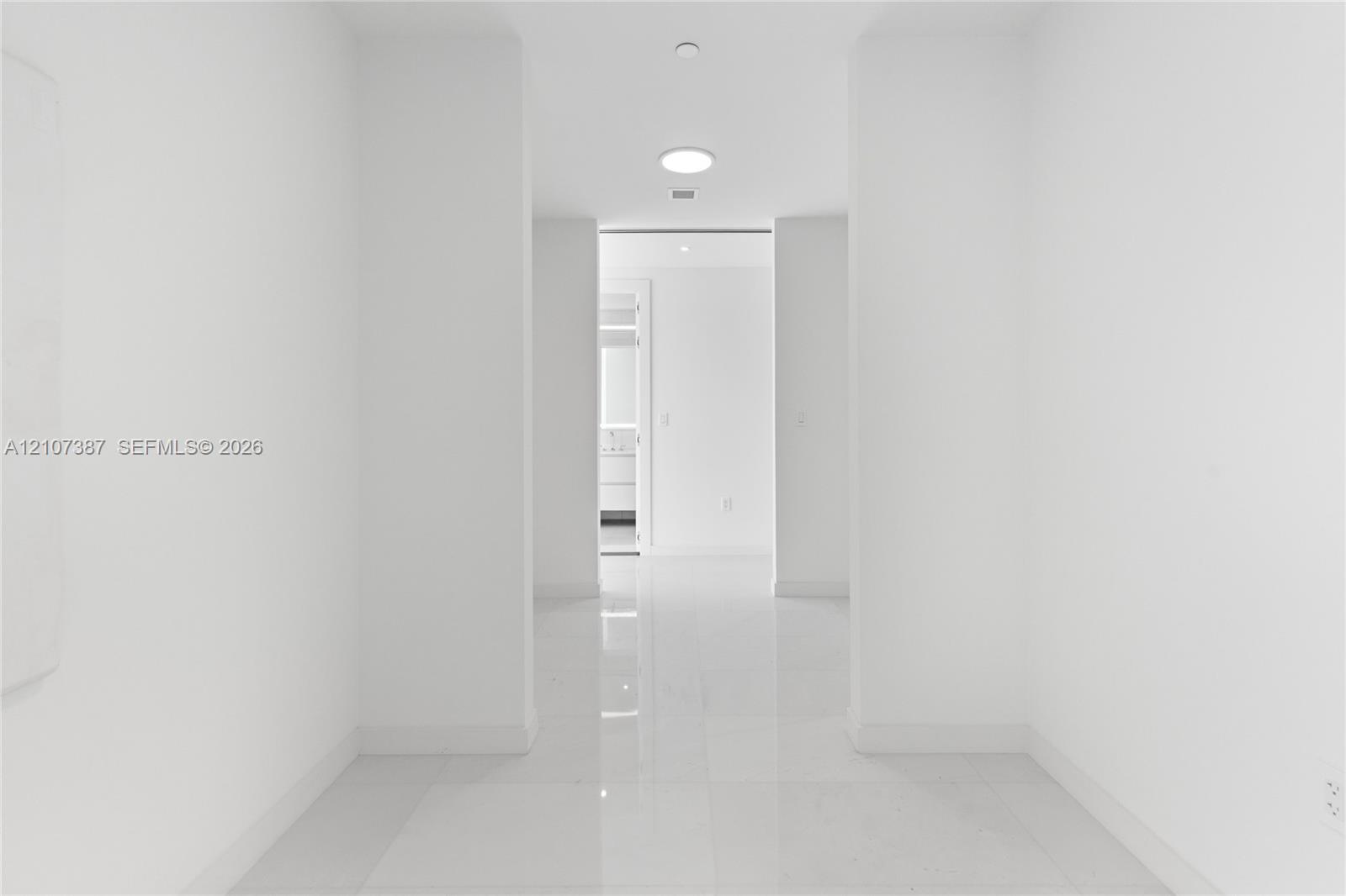 Interior corridor featuring polished stone-finish tile flooring, clean white walls, and recessed ceiling lighting