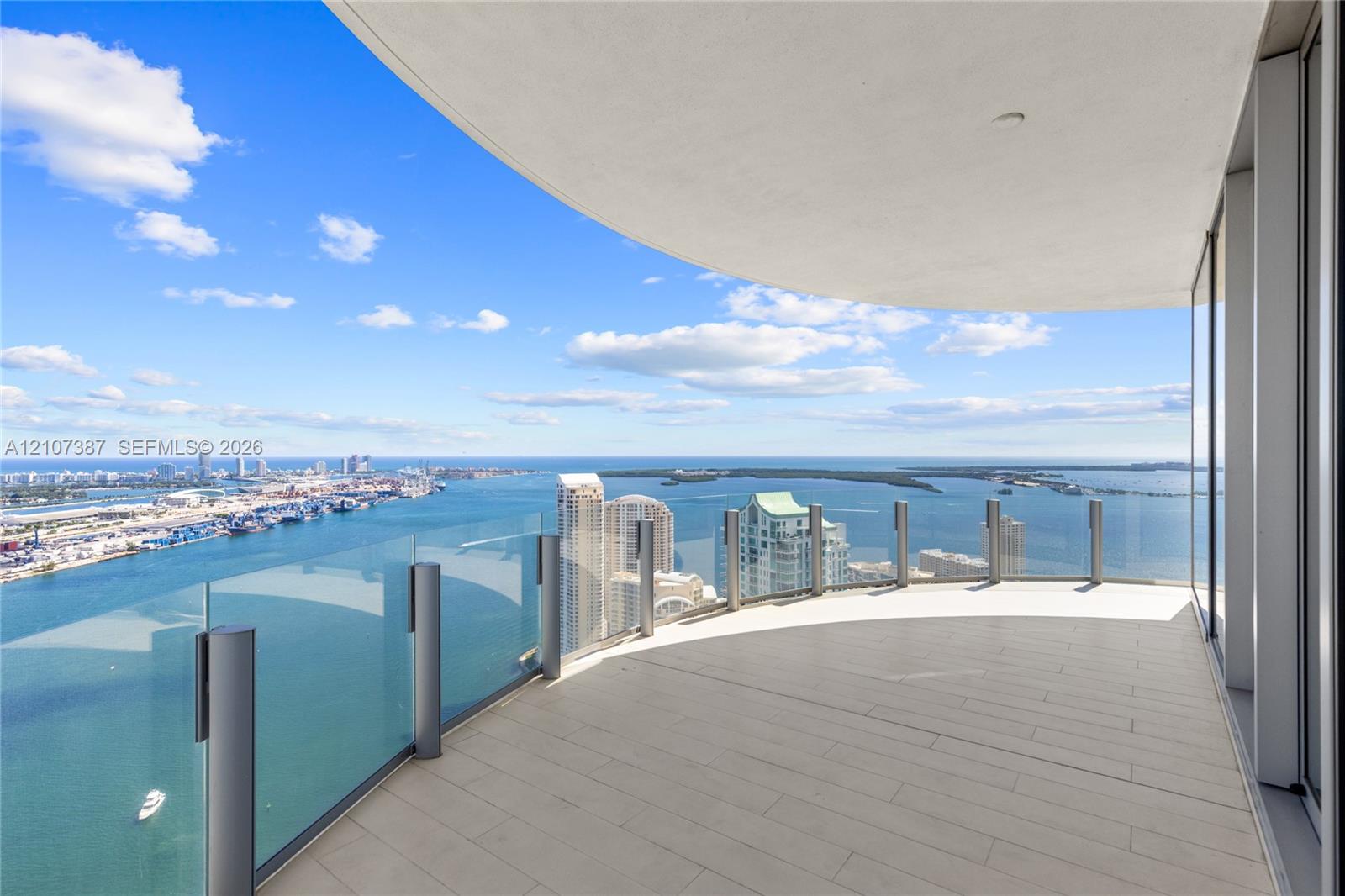 Curved balcony featuring tile flooring, glass panel railings, and panoramic coastal and urban scenery