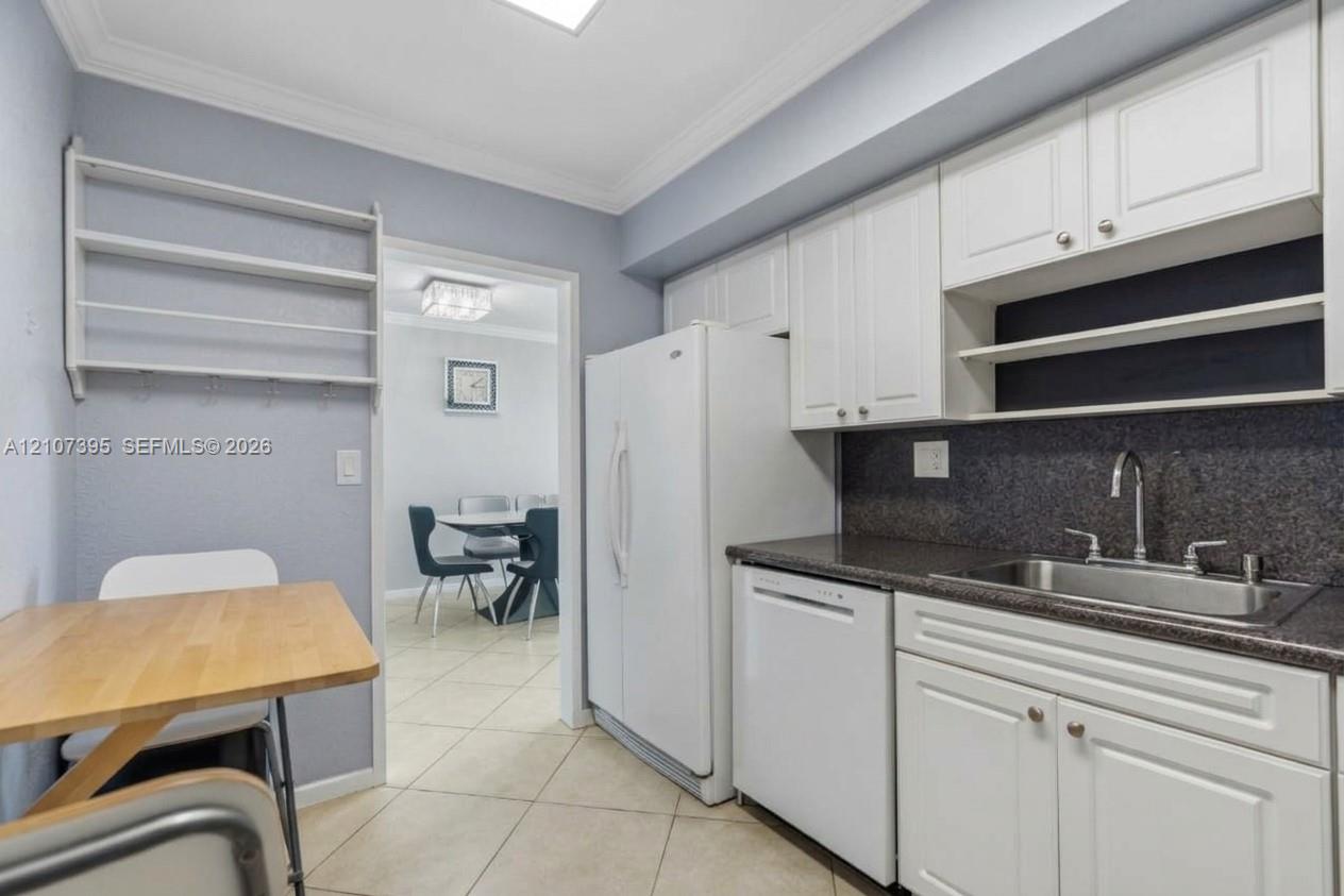 Kitchen featuring white raised-panel cabinetry, dark stone-finish countertops, stainless steel sink with gooseneck faucet, tile flooring, and built-in wall shelving