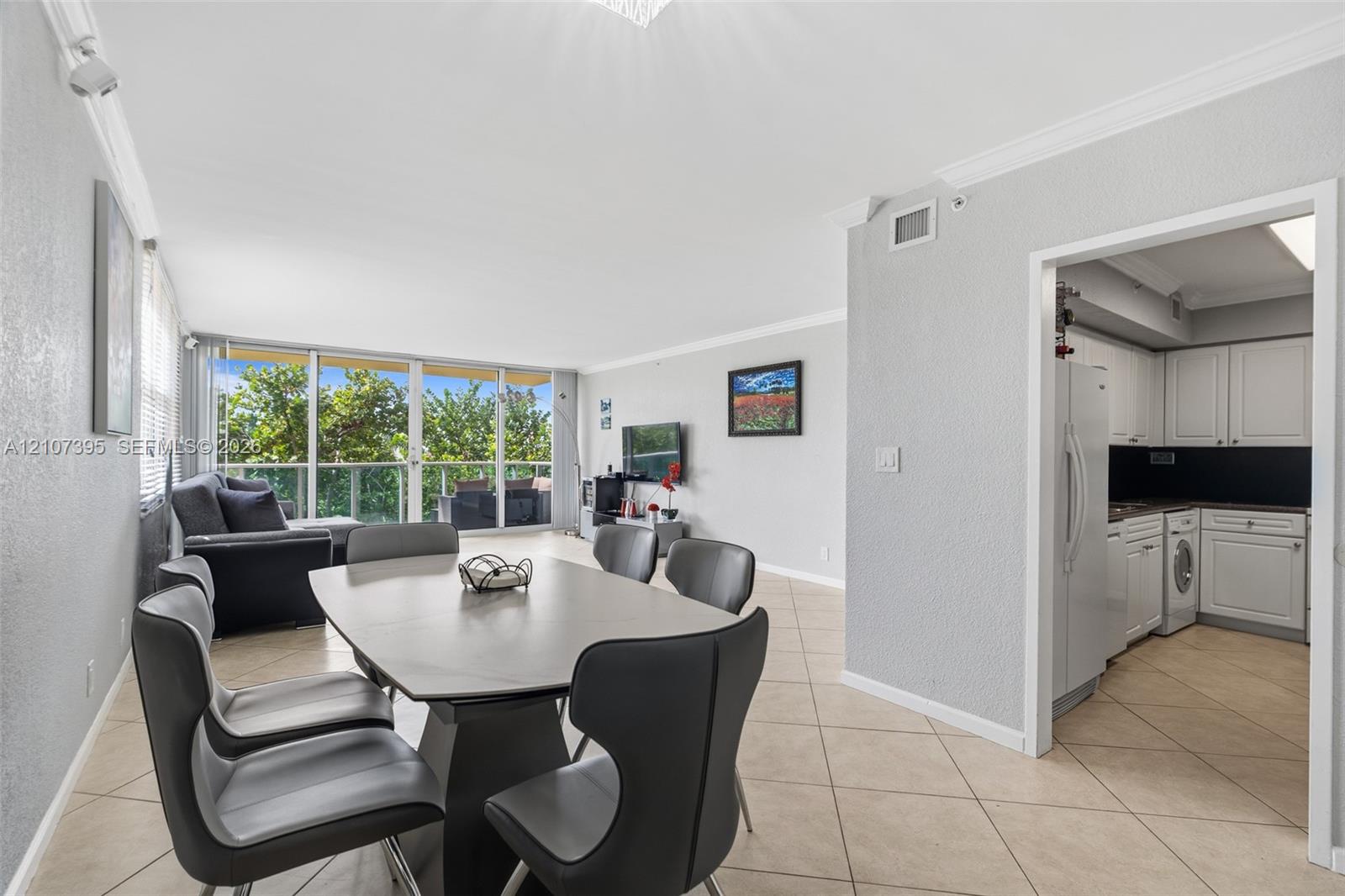 Open-concept interior featuring large floor-to-ceiling windows, tile flooring, crown molding, and white cabinetry in the kitchen