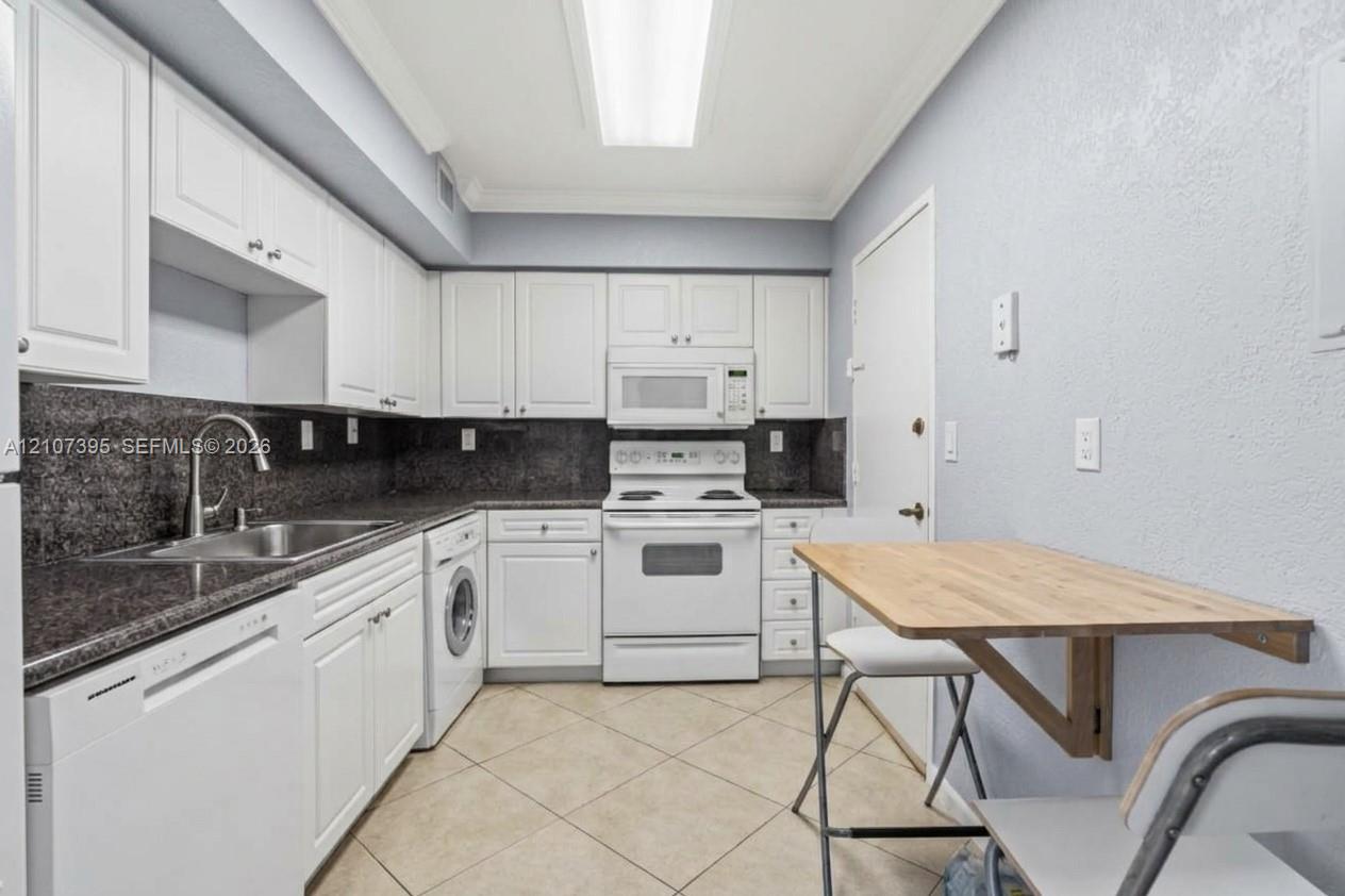 Kitchen featuring white cabinetry, dark stone-finish countertops, tile flooring, integrated appliances, and a mounted drop-leaf table