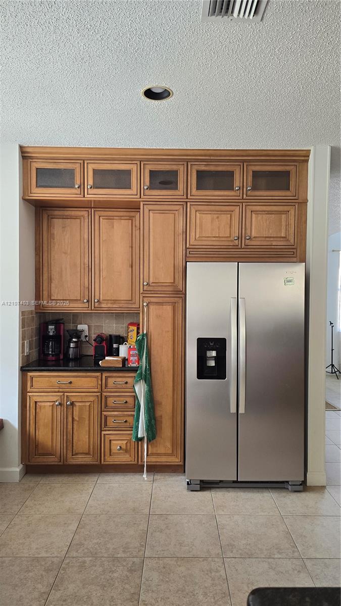 Custom built-in cabinetry featuring glass-panel upper doors, integrated stainless steel side-by-side refrigerator, stone-surfaced countertop, and tiled flooring