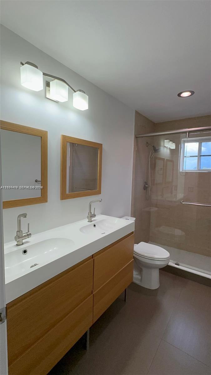 Dual-sink vanity with wood-finish cabinetry, rectangular under-mount basins, polished chrome fixtures, two wood-framed mirrors, and a glass-enclosed shower