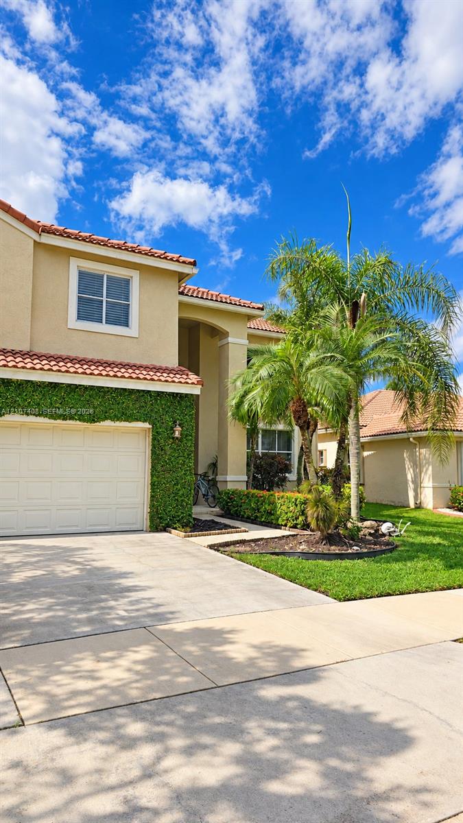 Stucco exterior with a tiled roof, integrated garage, concrete driveway, and manicured landscaping featuring mature palm trees Stucco exterior with a tiled roof, integrated garage, concrete driveway, and manicured landscaping featuring mature palm trees