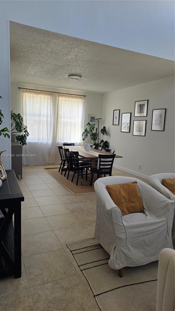 Open-concept living space featuring high vaulted ceilings, large windows with natural light, and neutral tile flooring throughout Open-concept living space featuring high vaulted ceilings, large windows with natural light, and neutral tile flooring throughout